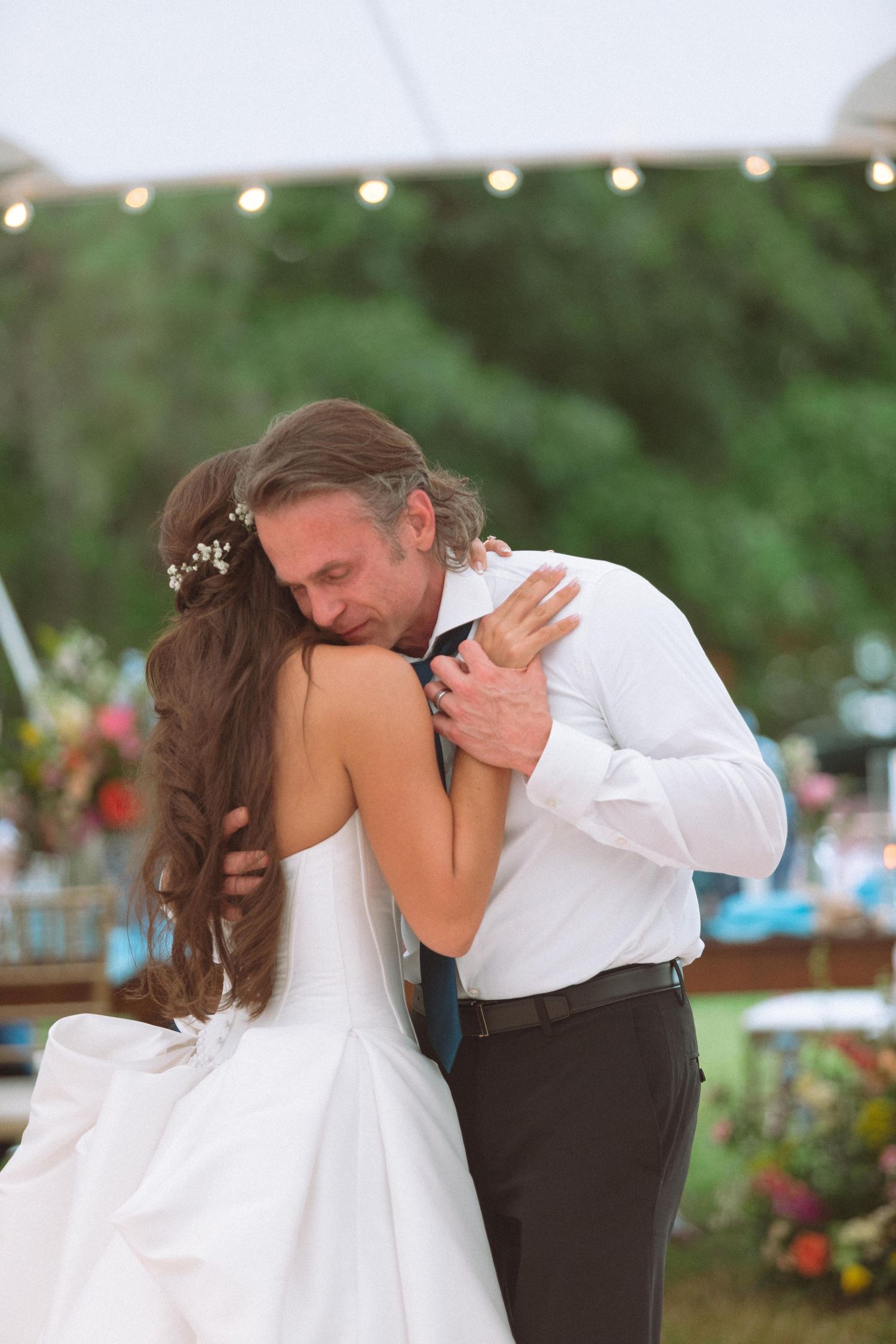 Bride and groom sharing an intimate first dance embrace under string lights at outdoor wedding reception.