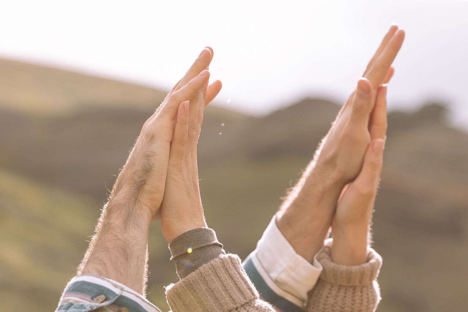 Close-up of two people pressing their hands together against a soft mountain backdrop.