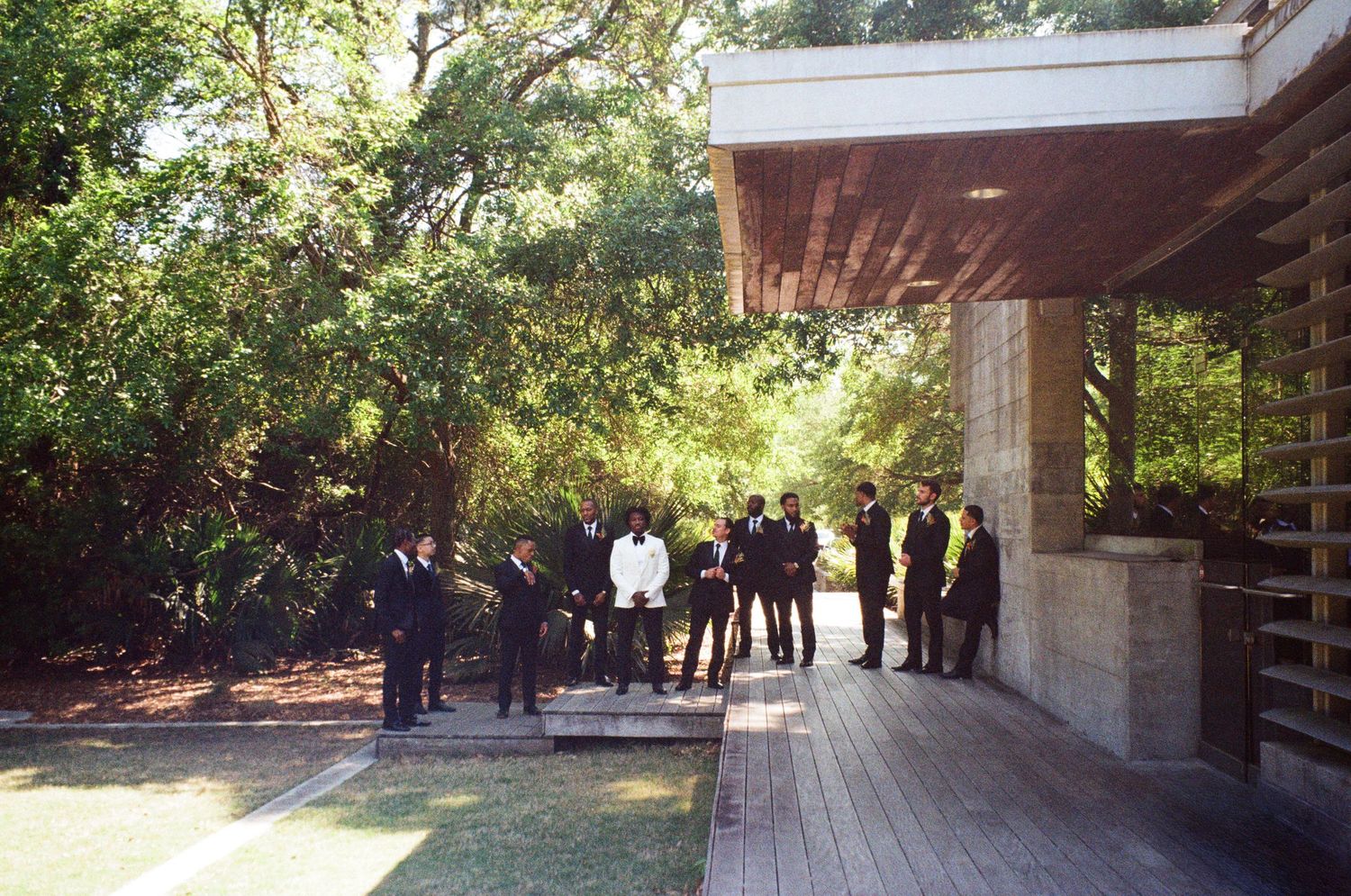 Groomsmen gathered on a wooden deck surrounded by lush trees at an outdoor wedding venue.
