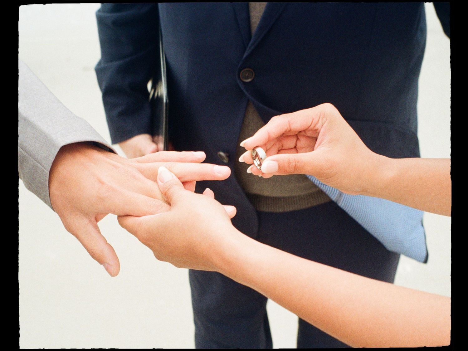 Close-up of bride placing a wedding ring on grooms finger during an outdoor ceremony.