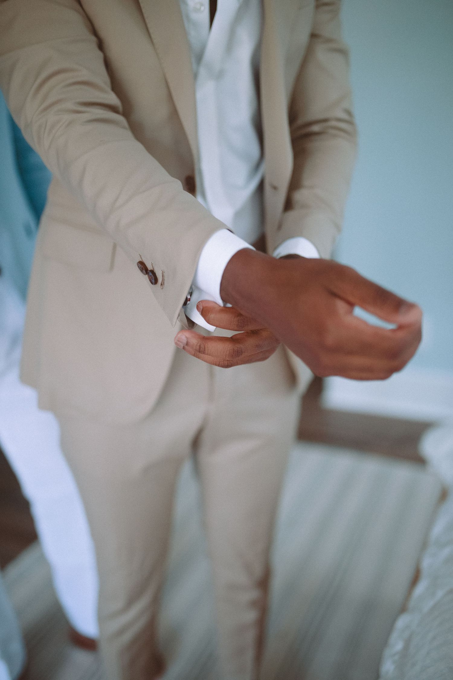 Close-up of groom in beige suit adjusting his cufflinks while getting ready for his wedding.