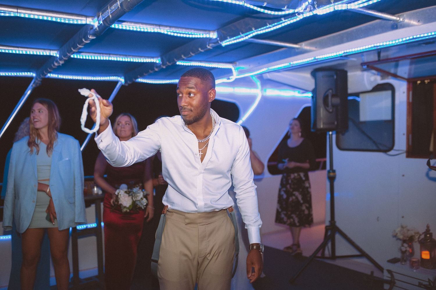 Groom holding garter up triumphantly at fun wedding reception with neon blue lights.