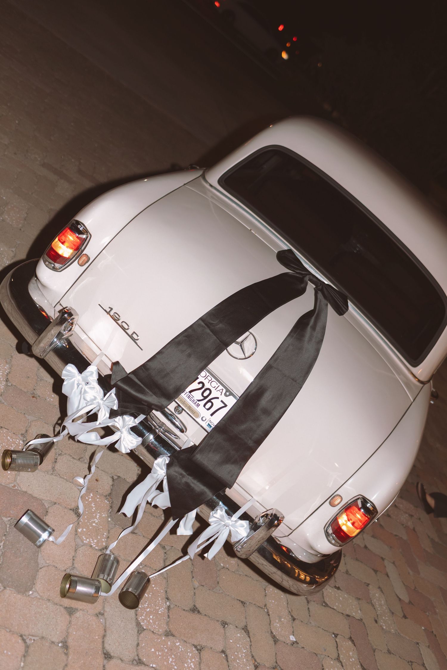 Rear view of vintage white Mercedes wedding car decorated with tin cans and white ribbons at night.