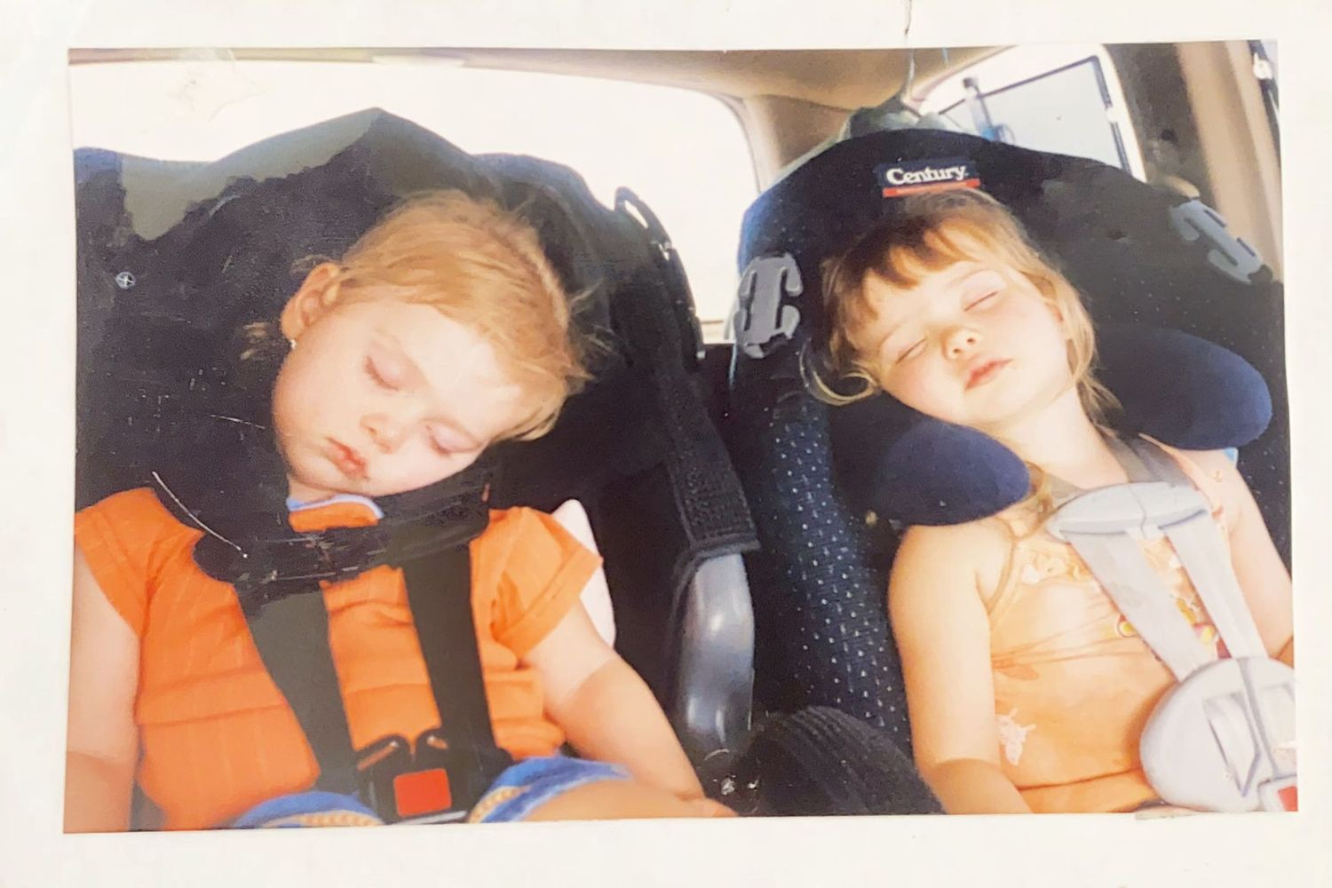 Two young children sleeping in car seats during a road trip.