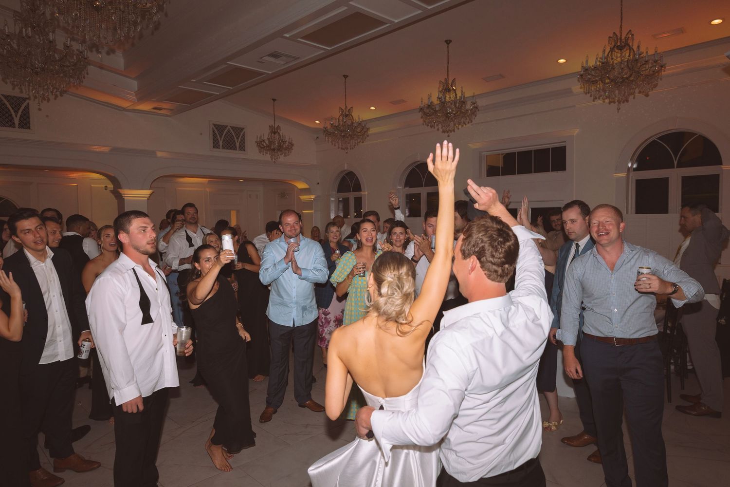 Bride and groom share a joyful dance surrounded by cheering guests in an elegant ballroom reception.