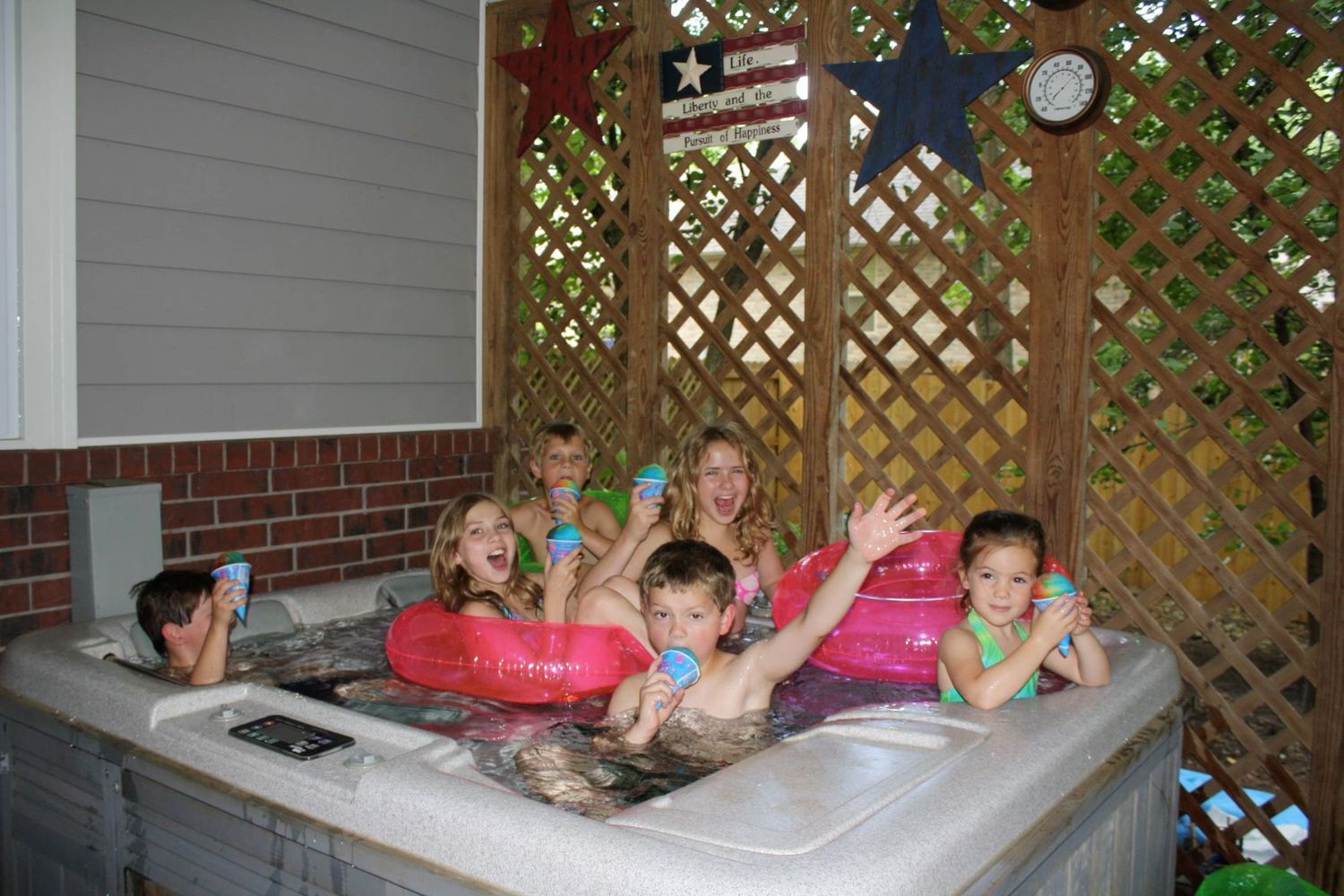 Happy group of children and an adult splashing and playing in an outdoor hot tub on a sunny day.