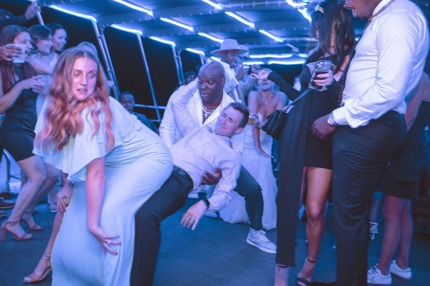 Wedding guests dancing and having fun at a lively reception with blue neon lighting.