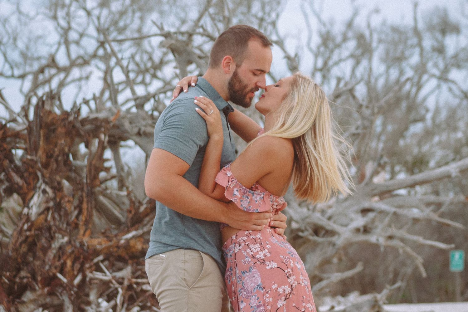 Couple embracing and almost kissing surrounded by driftwood on a Florida beach.
