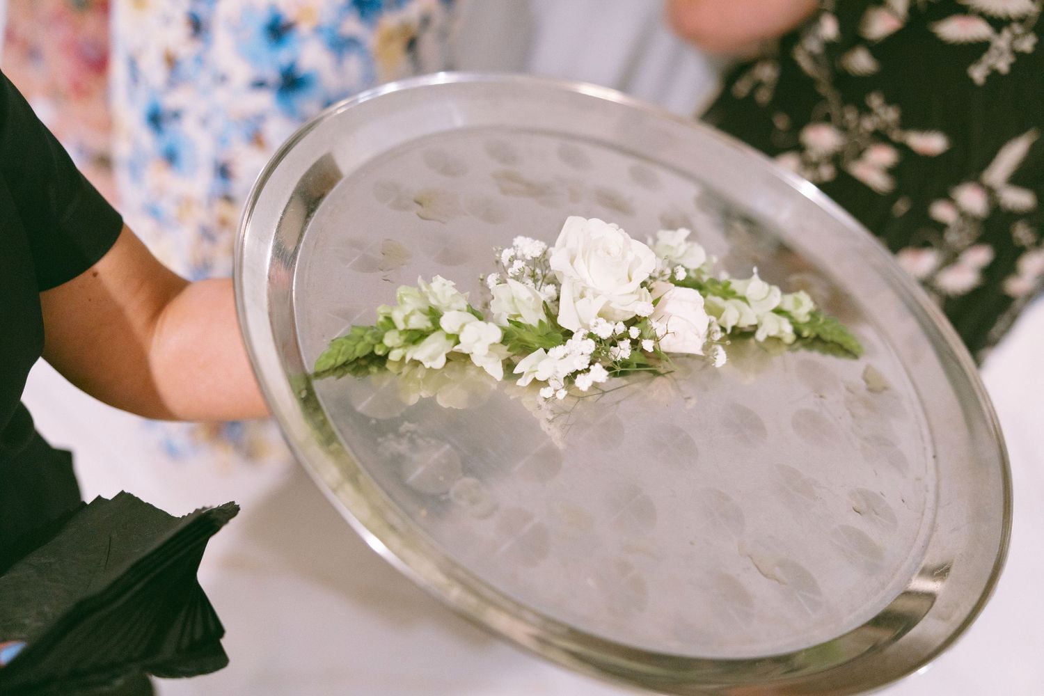 Silver tray holding two white rose boutonnieres with greenery for a wedding ceremony.