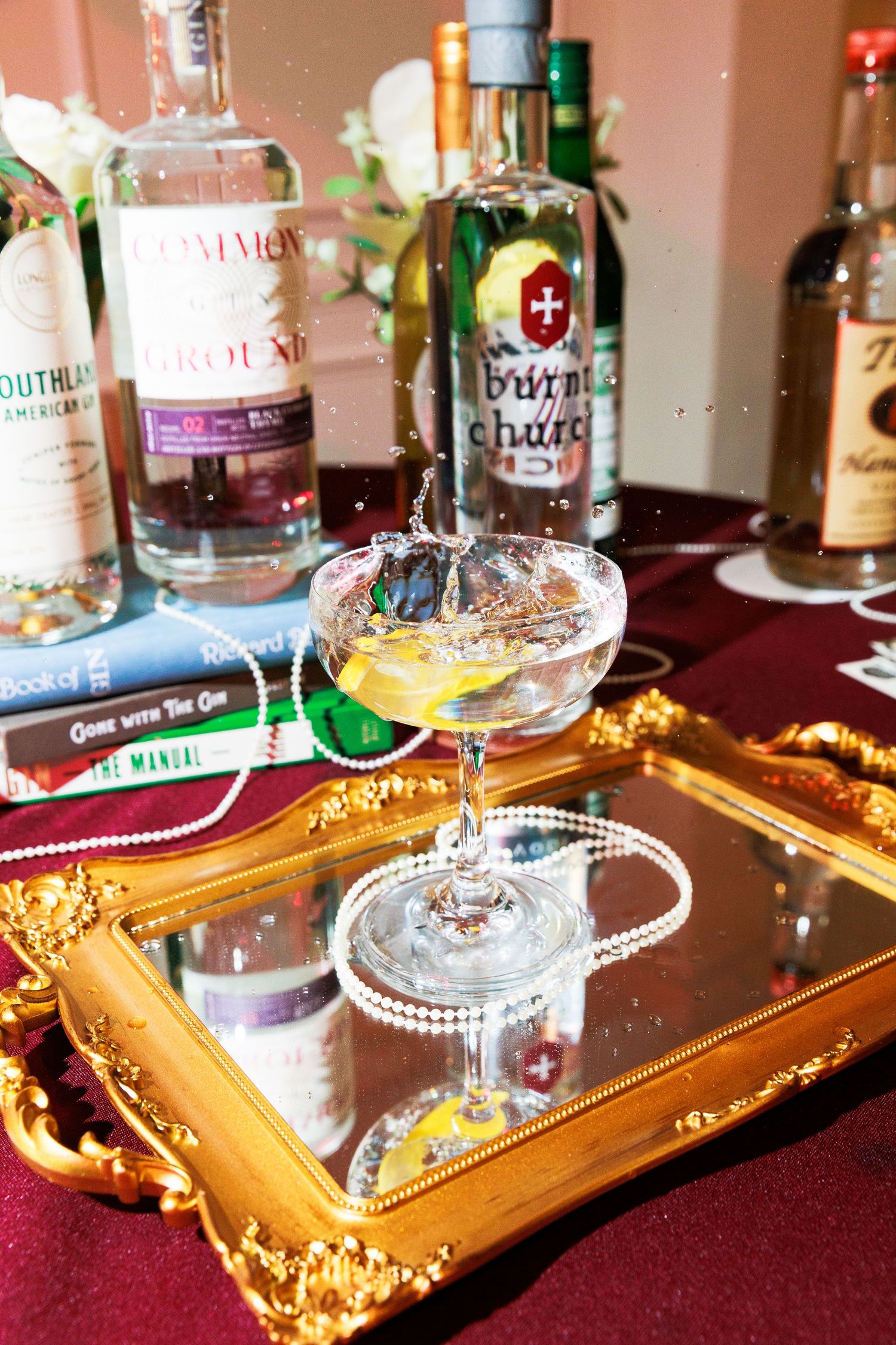Elegant martini cocktail with lemon garnish on a gold mirrored tray surrounded by premium spirit bottles.