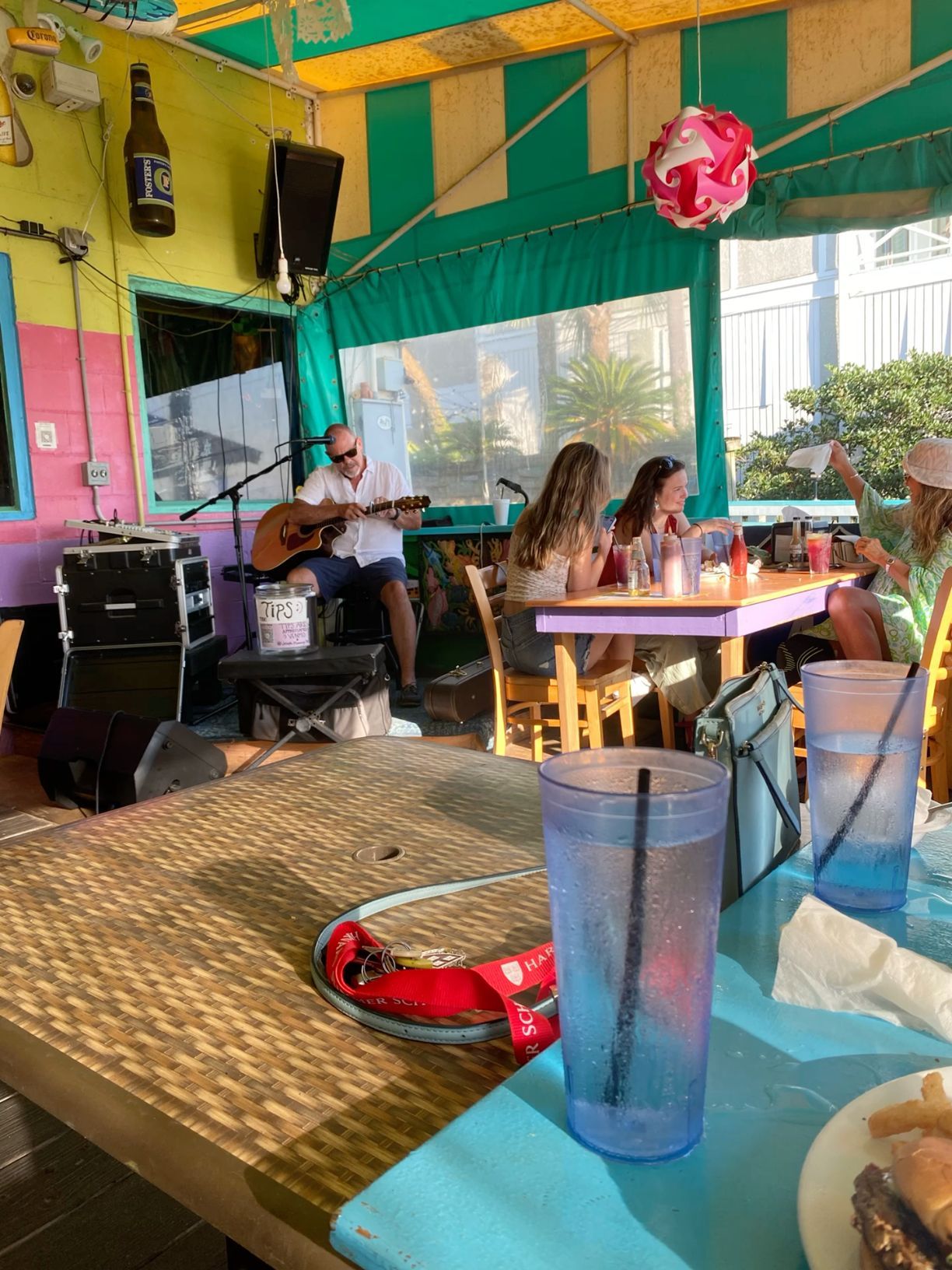 Live musician playing guitar at a colorful outdoor restaurant patio with guests dining nearby.