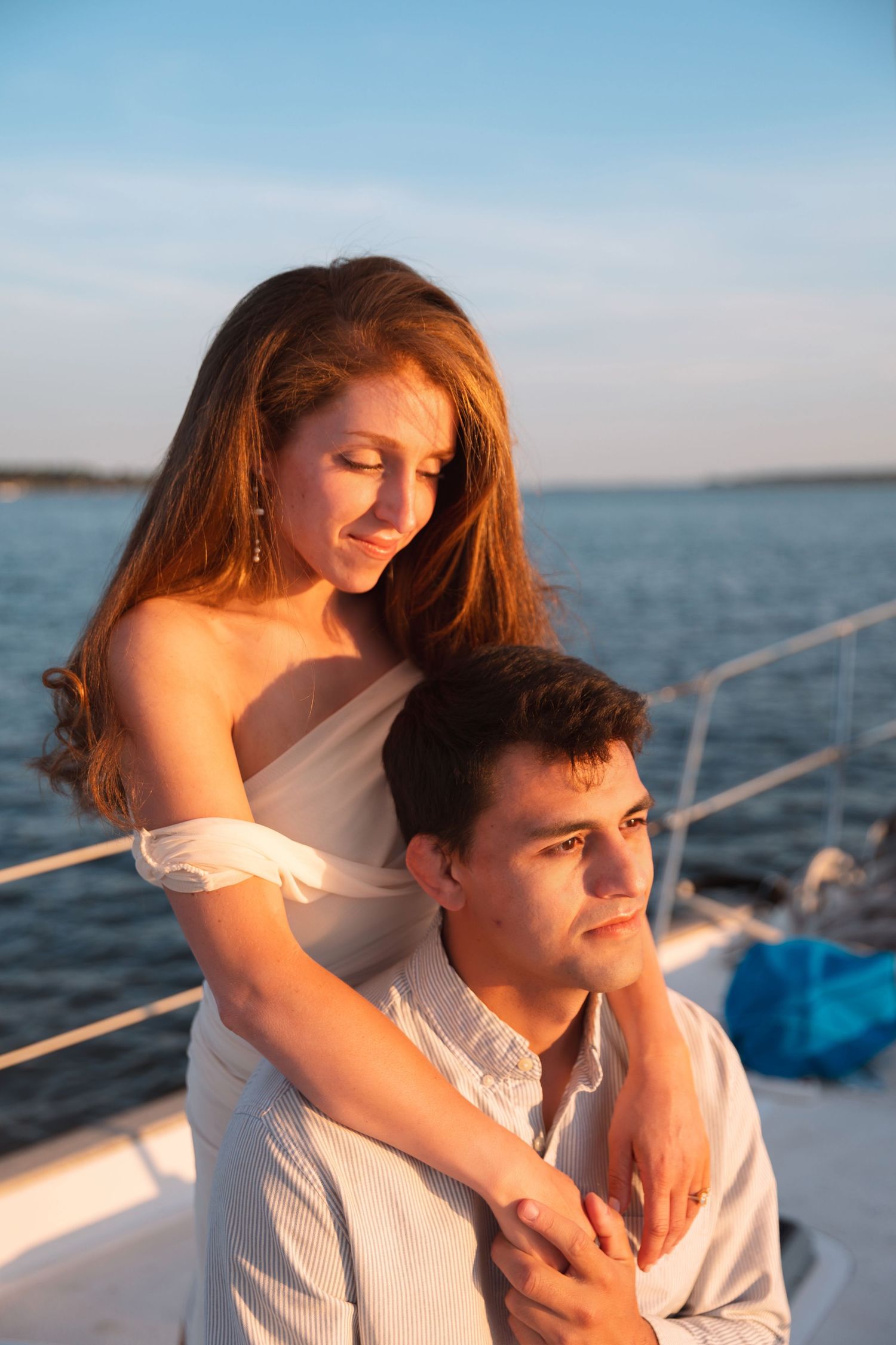 Young couple in white embracing on a yacht at golden sunset over calm ocean waters.
