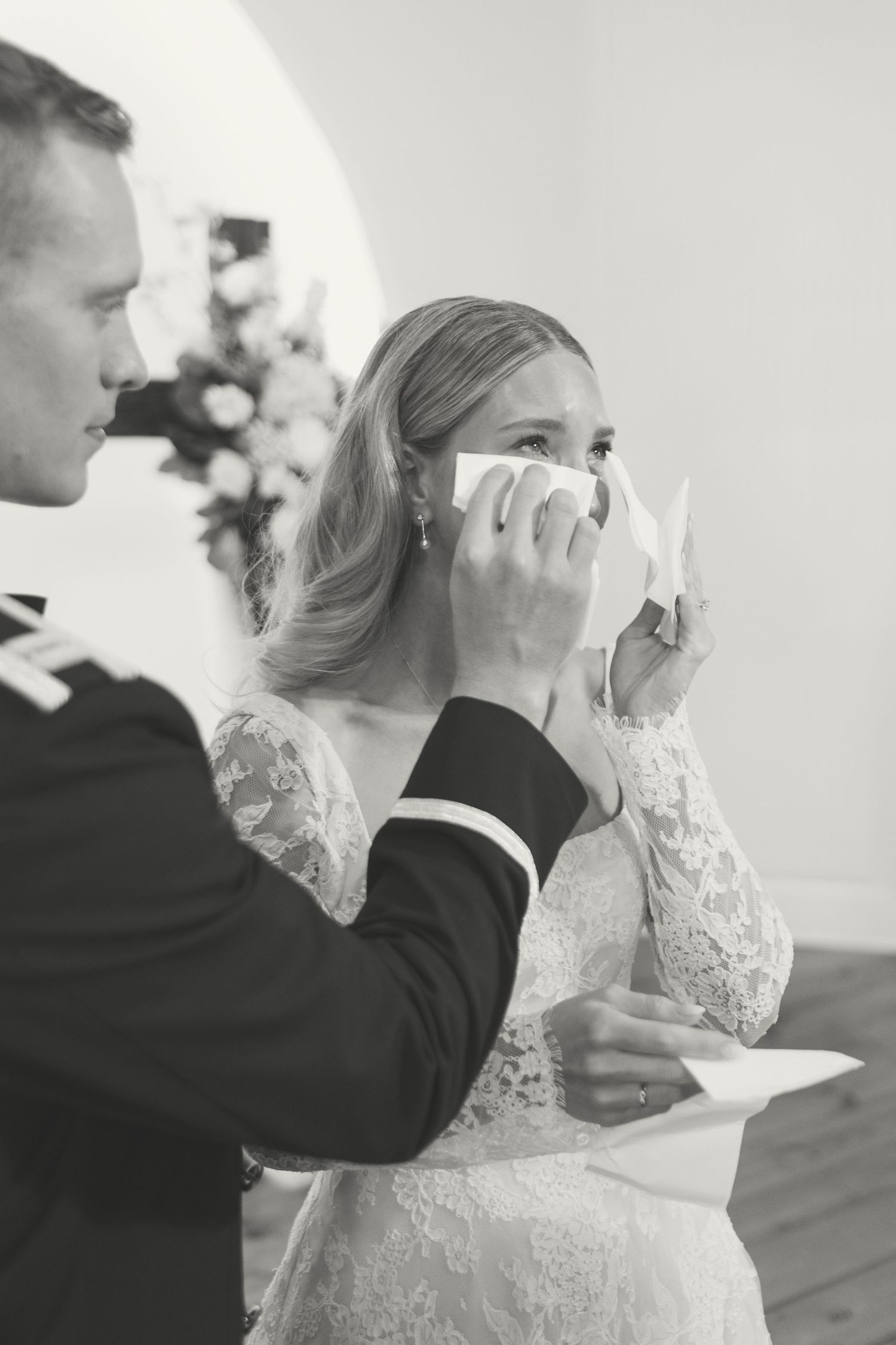 Emotional bride dabs tears with handkerchief during wedding vows ceremony in black and white.