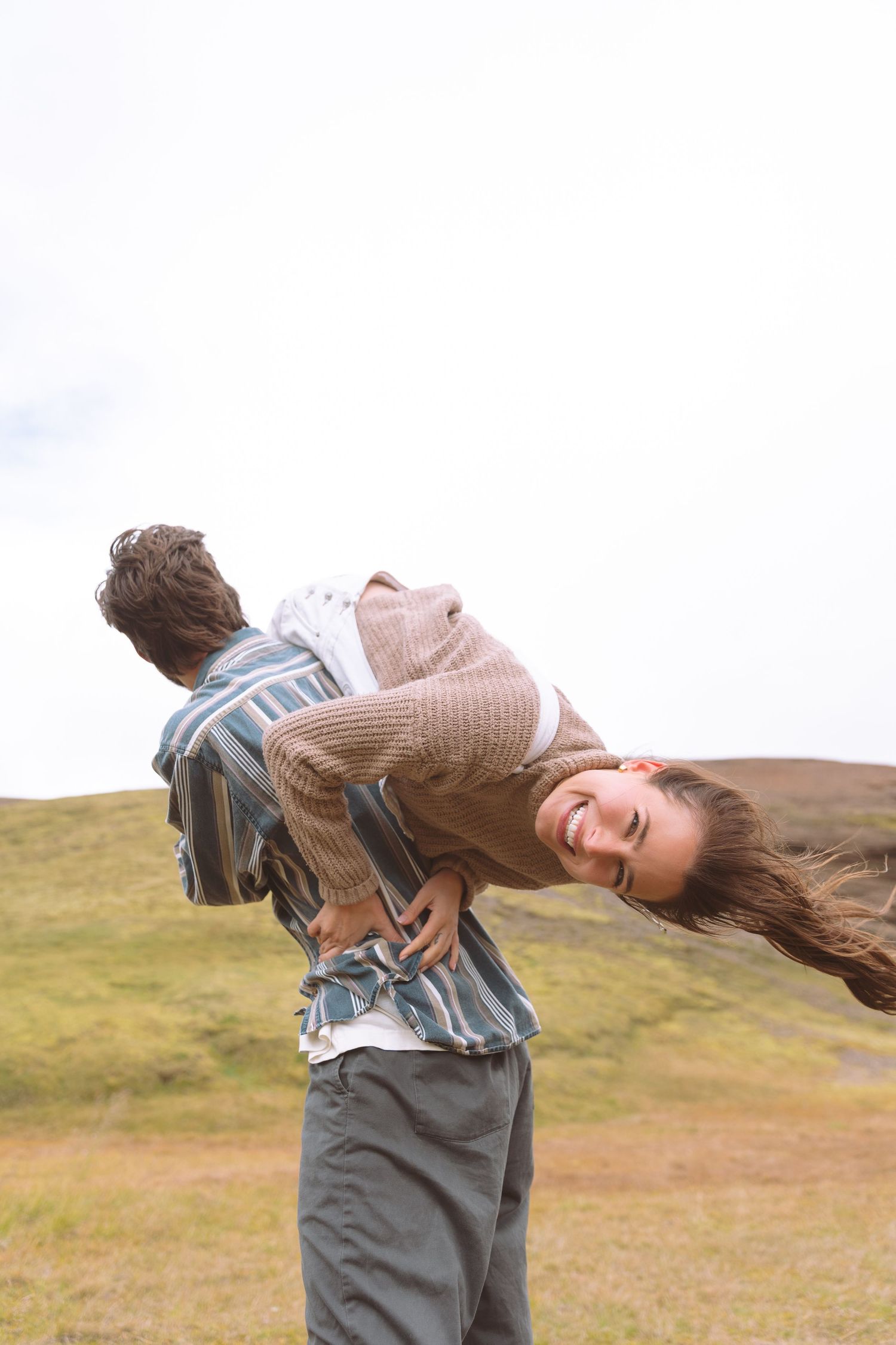 Joyful woman laughing while being carried on a mans back in a scenic green Icelandic highland landscape.