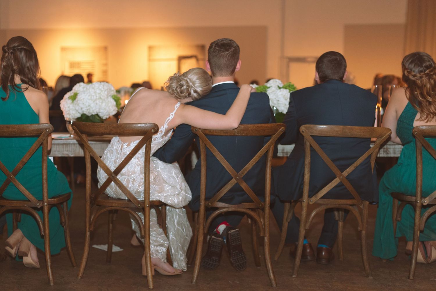 Bride and groom sitting closely together at wedding reception table with white floral centerpieces.