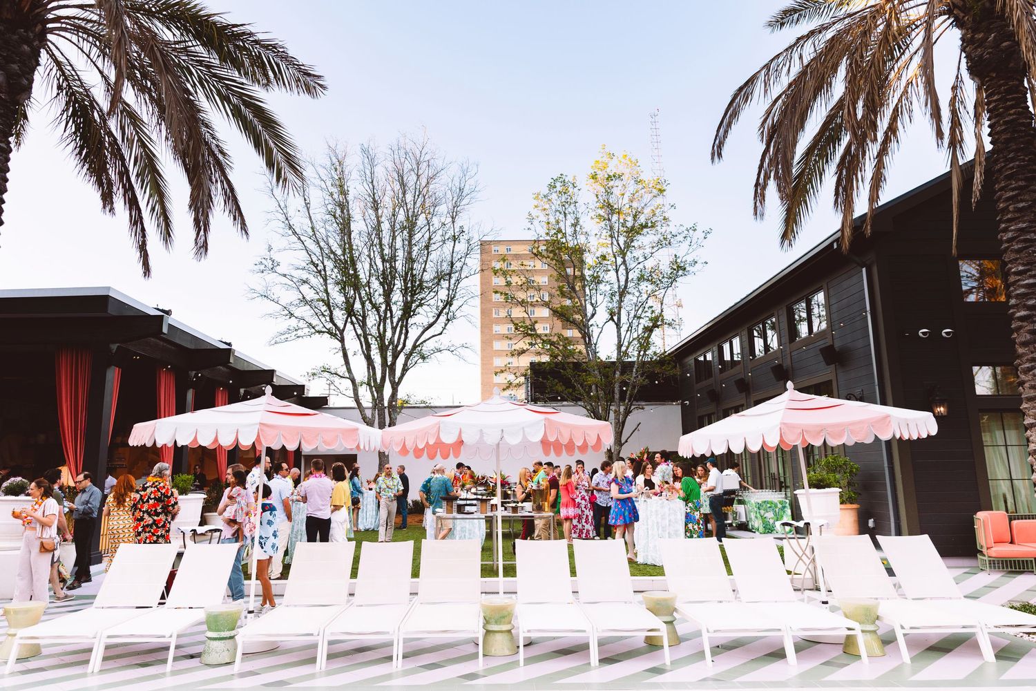 Outdoor poolside event with white lounge chairs, pink umbrellas, and palm trees at an elegant venue.
