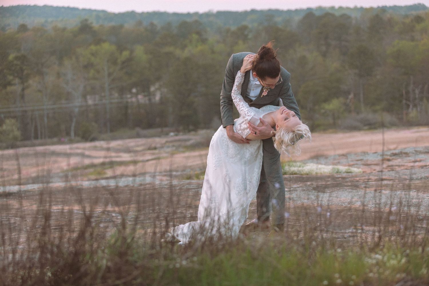 Bride and groom sharing a romantic dip kiss in an outdoor rustic landscape at dusk.