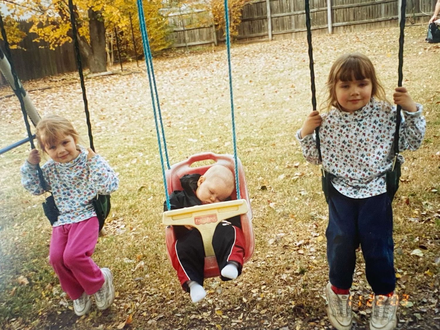 Three young children playing on swings in a backyard during autumn.