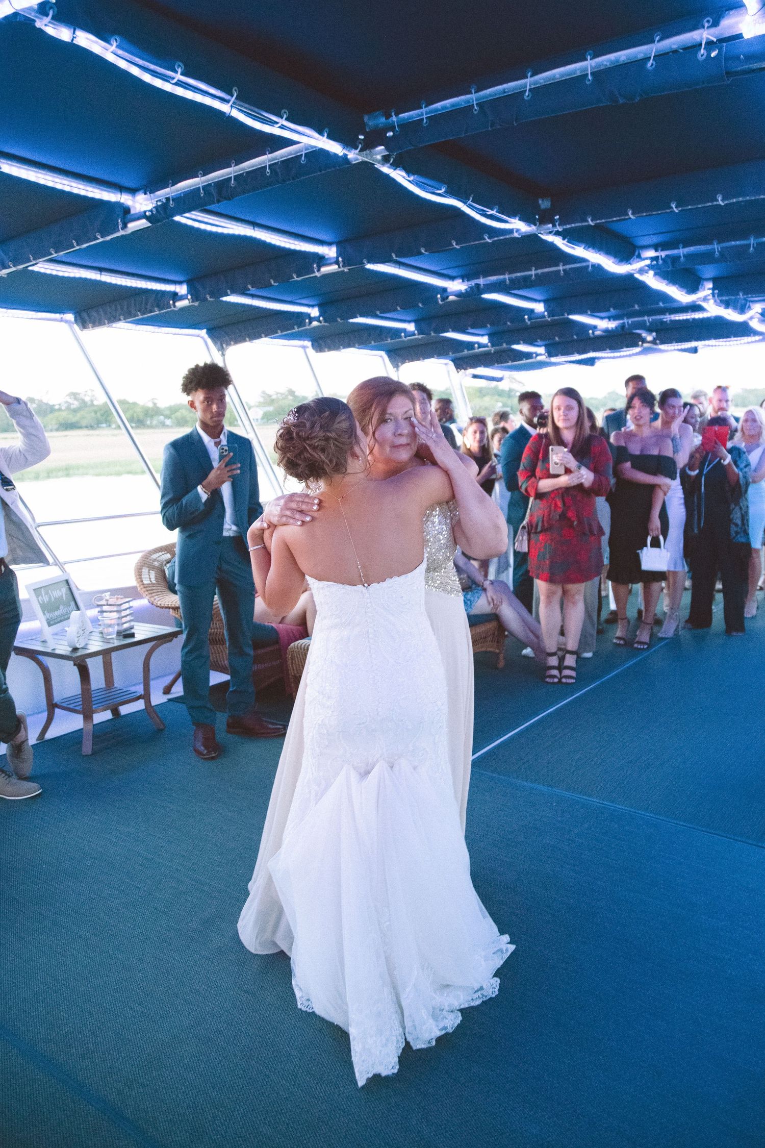 Bride and guest share a tender dance moment at an outdoor boat wedding reception.