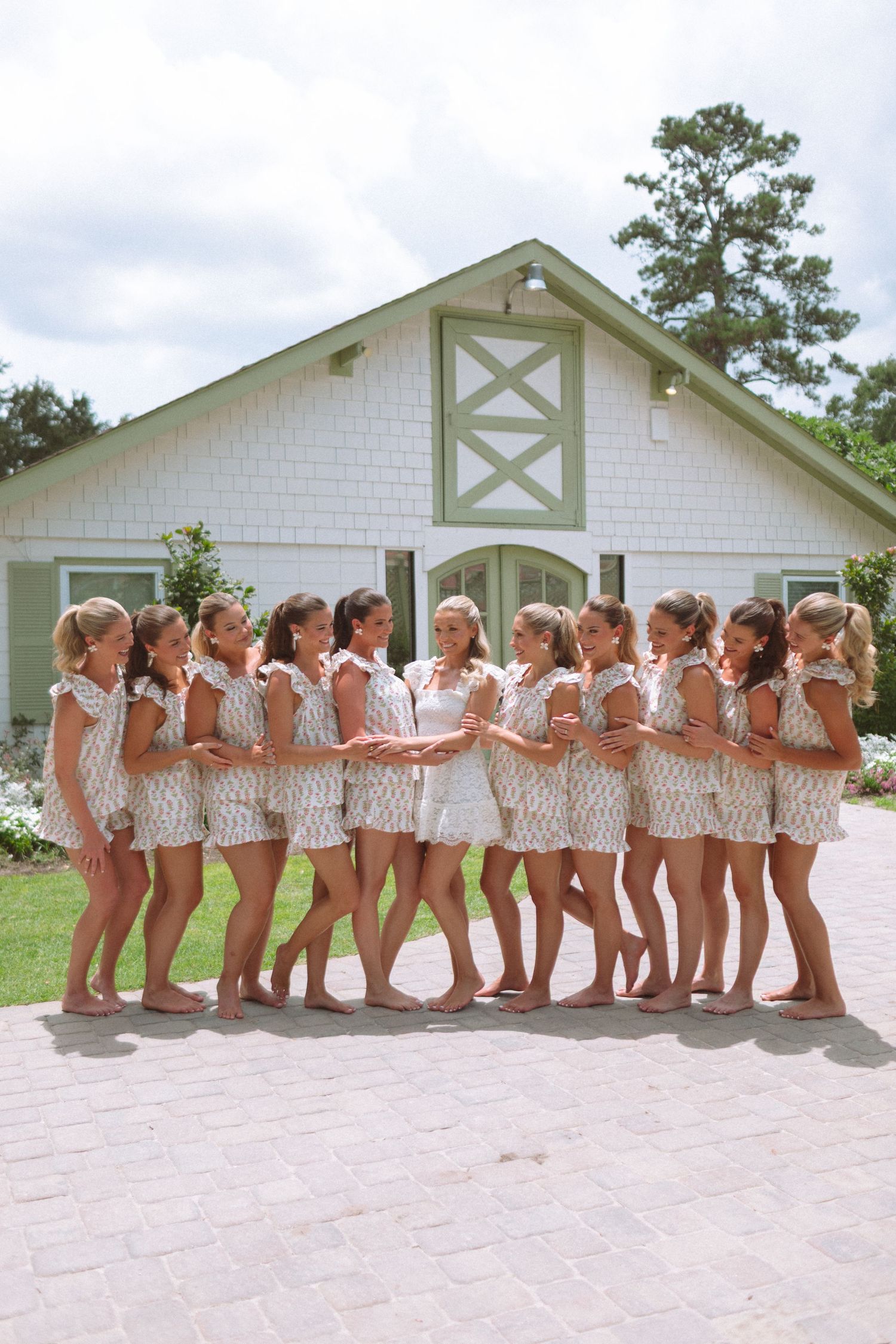 Bridesmaids pose in matching patterned pajamas outside a white barn venue before the wedding.