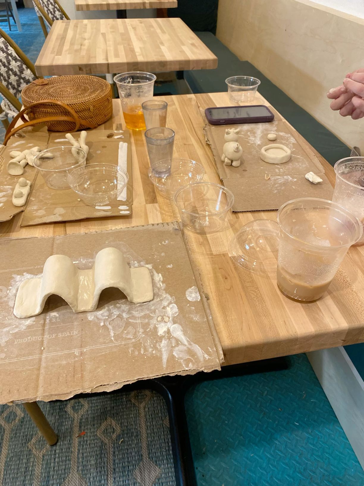 Pottery class workspace with clay pieces and drinks on wooden tables.