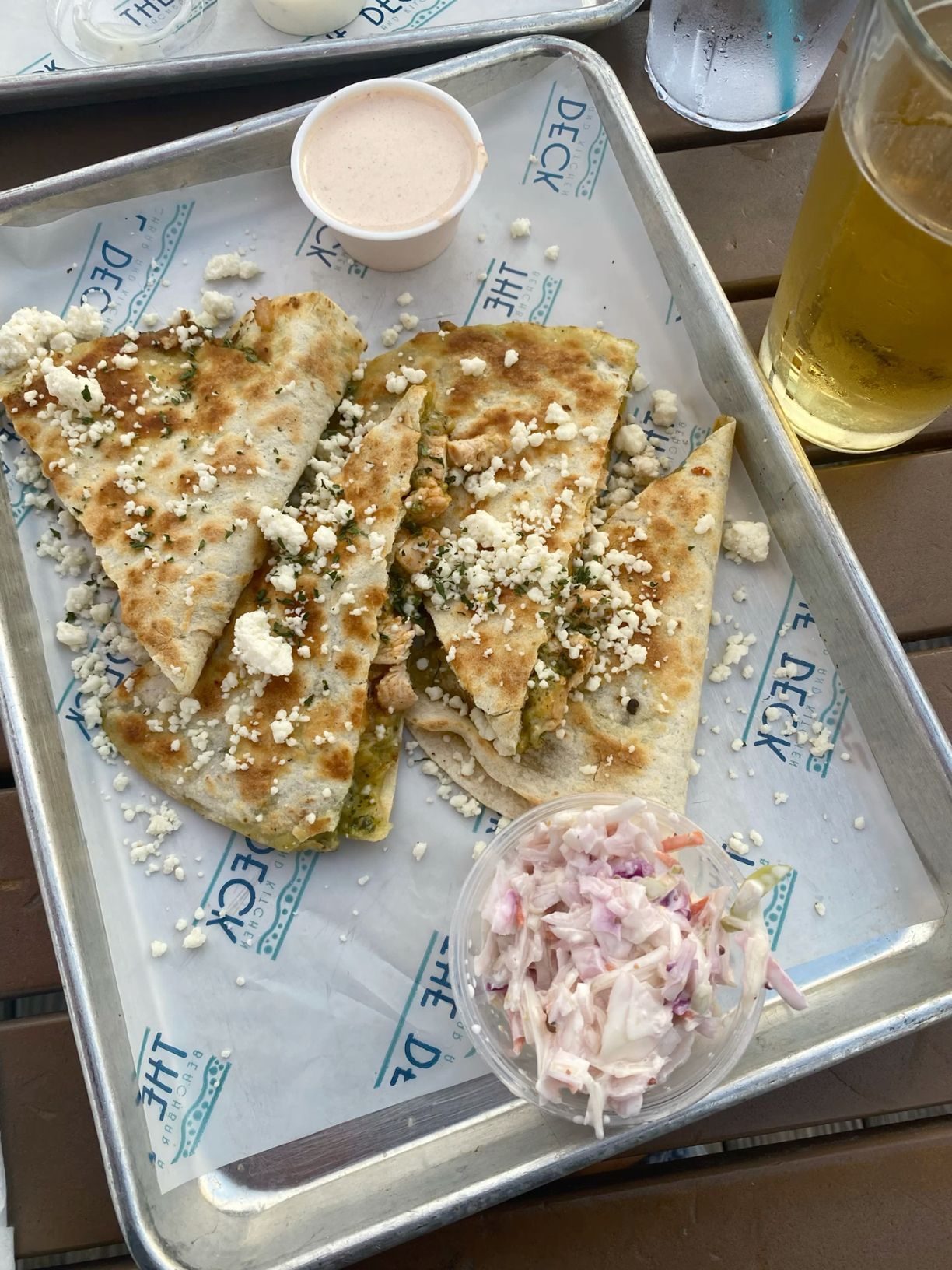 Quesadillas topped with cotija cheese served on metal tray with coleslaw and beer.