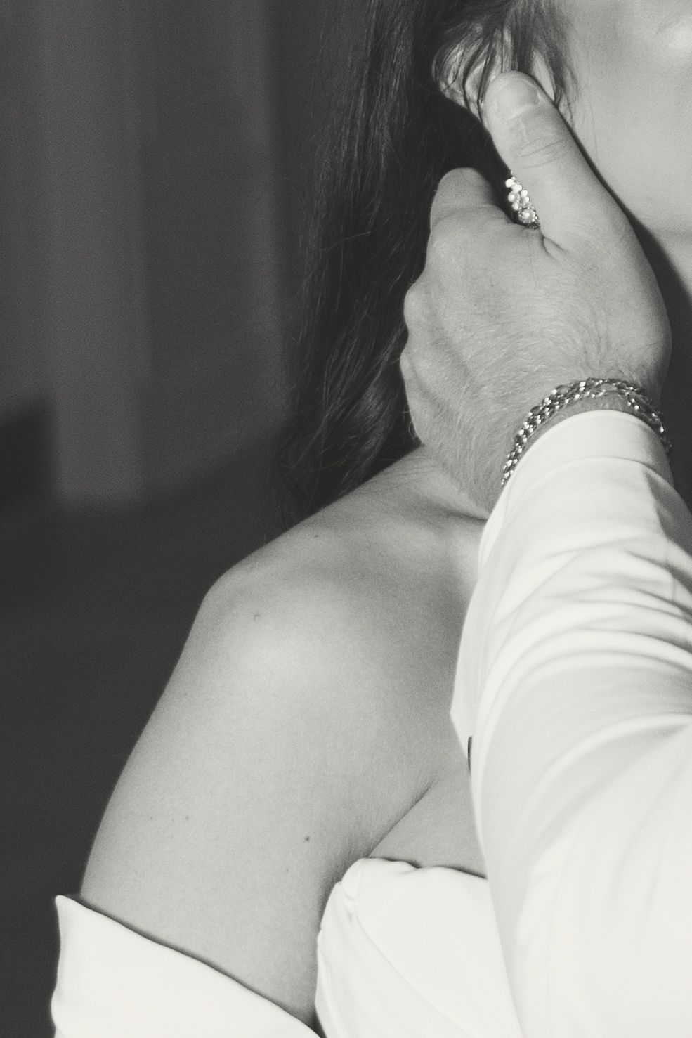Black and white close-up of a bride adjusting her earring, wearing a diamond bracelet and white wedding dress.