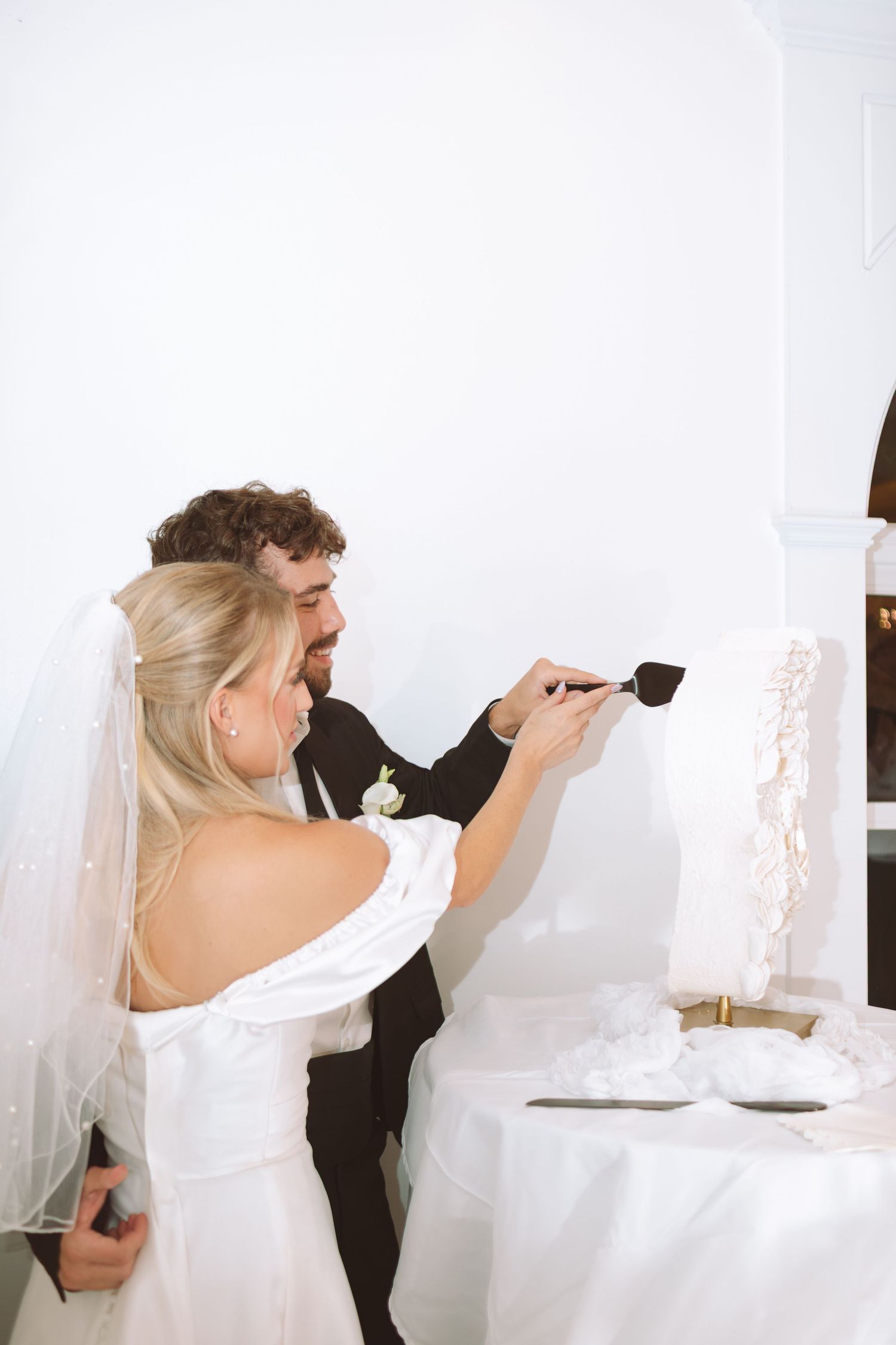 Bride and groom cutting their elegant white wedding cake together in a bright, beautifully decorated venue.