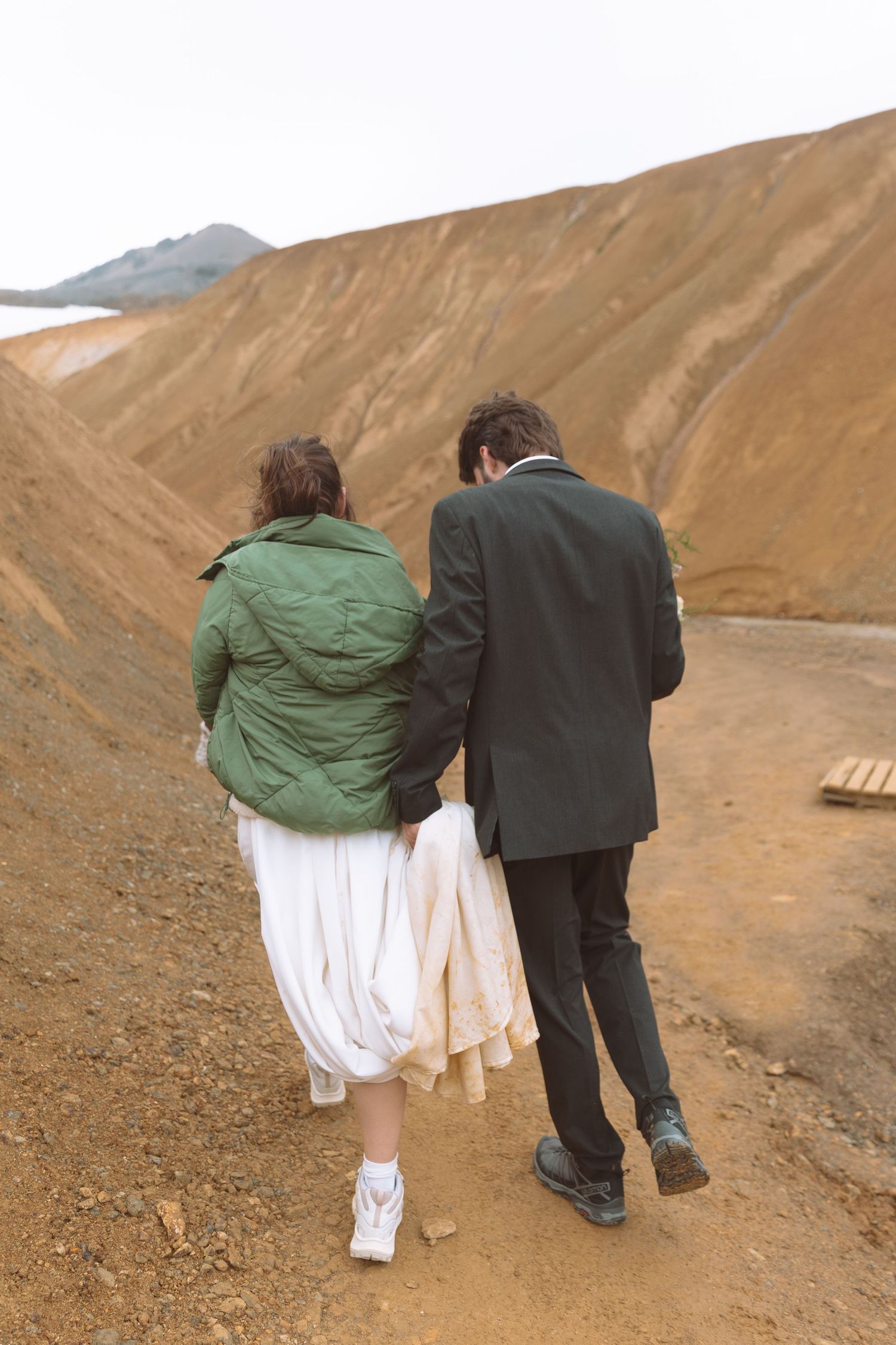 Bride and groom walk arm in arm along a dirt path through Iceland's striking orange volcanic terrain.