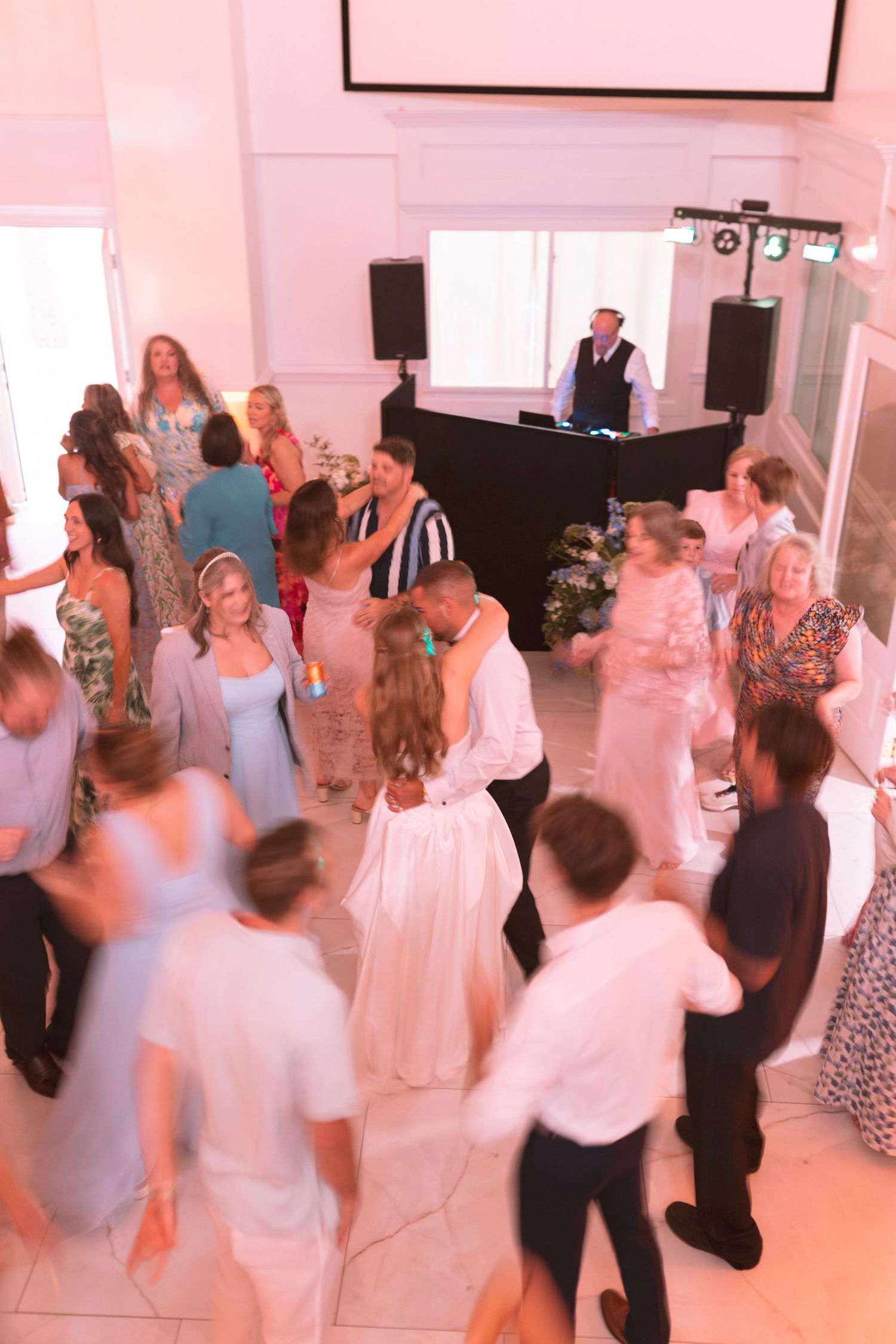 Aerial view of wedding reception dance floor filled with guests dancing under warm pink lights.