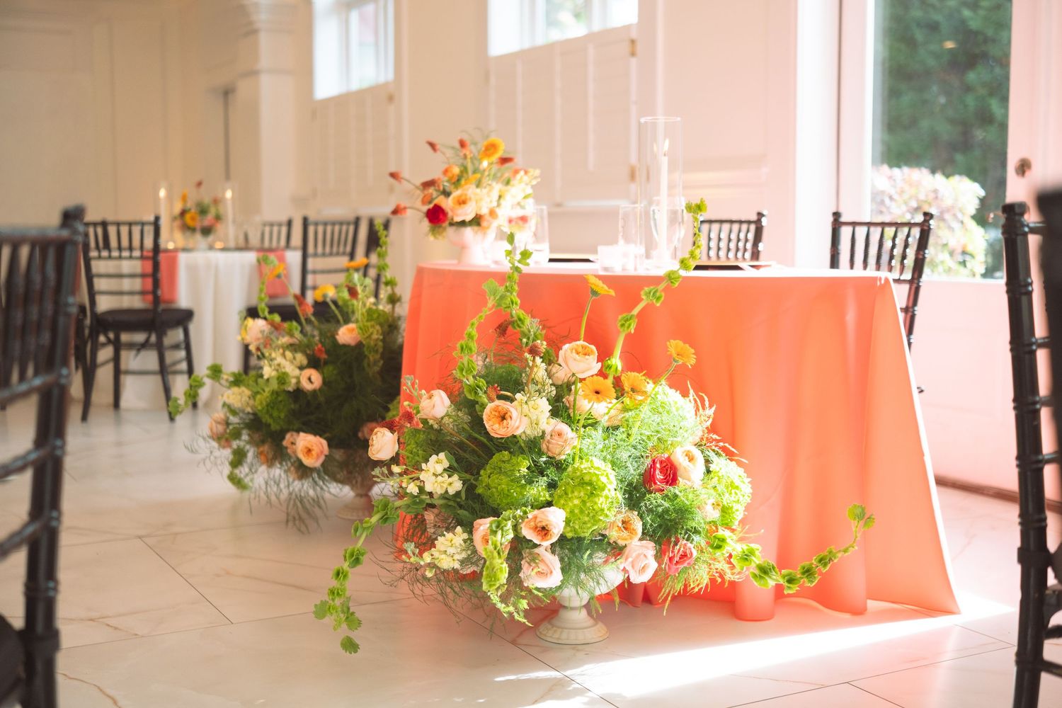 Elegant wedding reception table with coral linens and lush floral centerpieces featuring peach and green blooms.