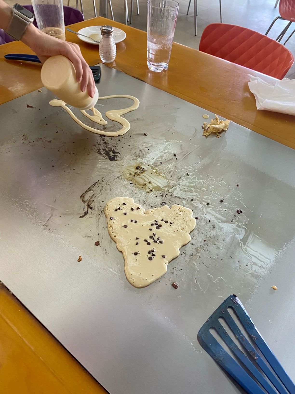 Pancake batter being poured into a heart shape on a hot griddle with chocolate chips.