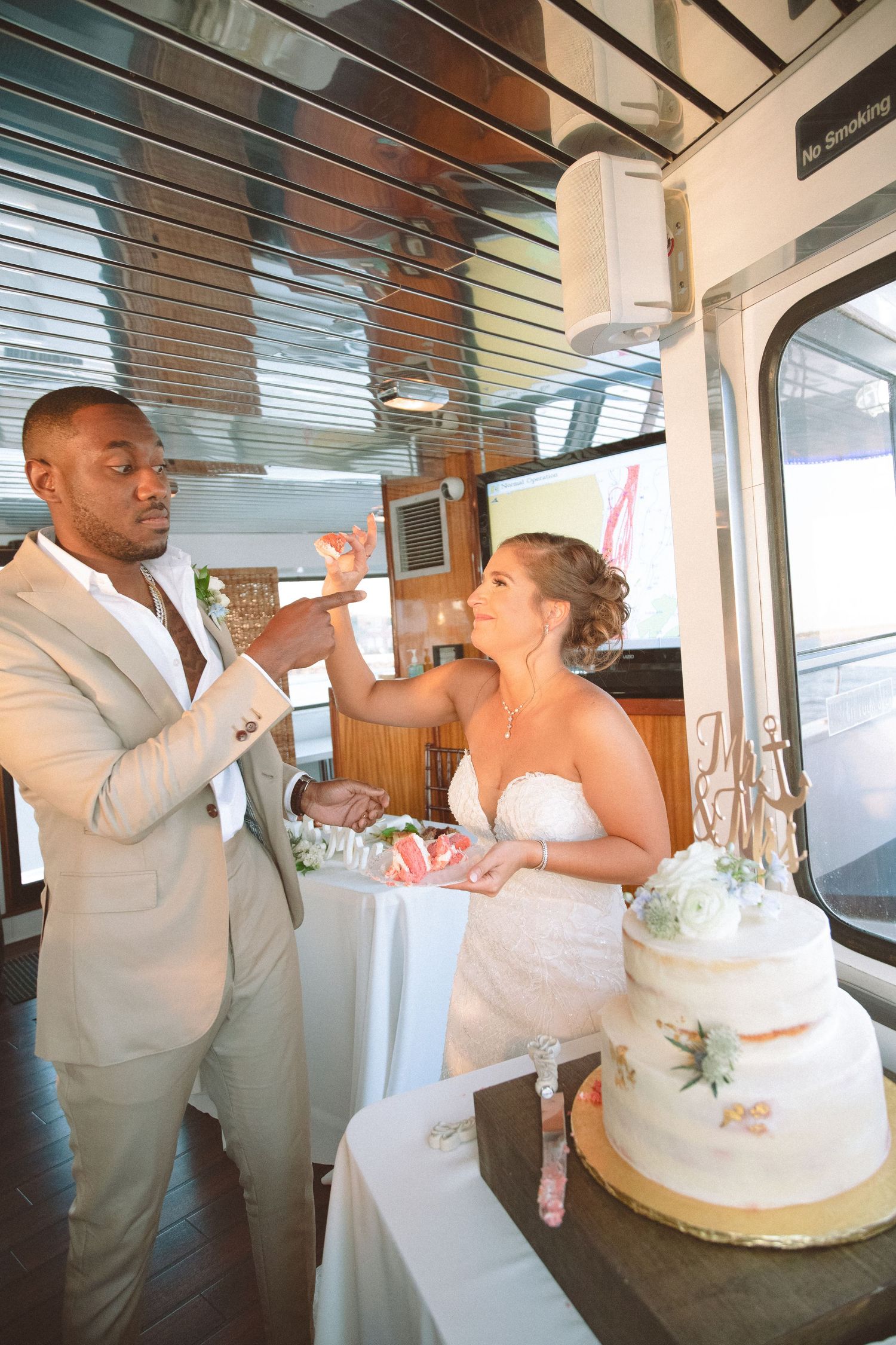 Playful bride and groom sharing cake at reception aboard a boat, groom catching piece mid-air.