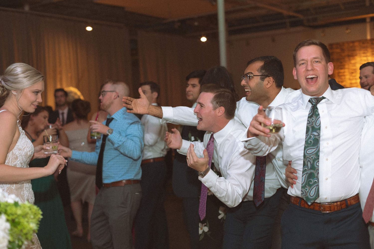 Wedding guests laugh and dance together at lively indoor reception celebration.