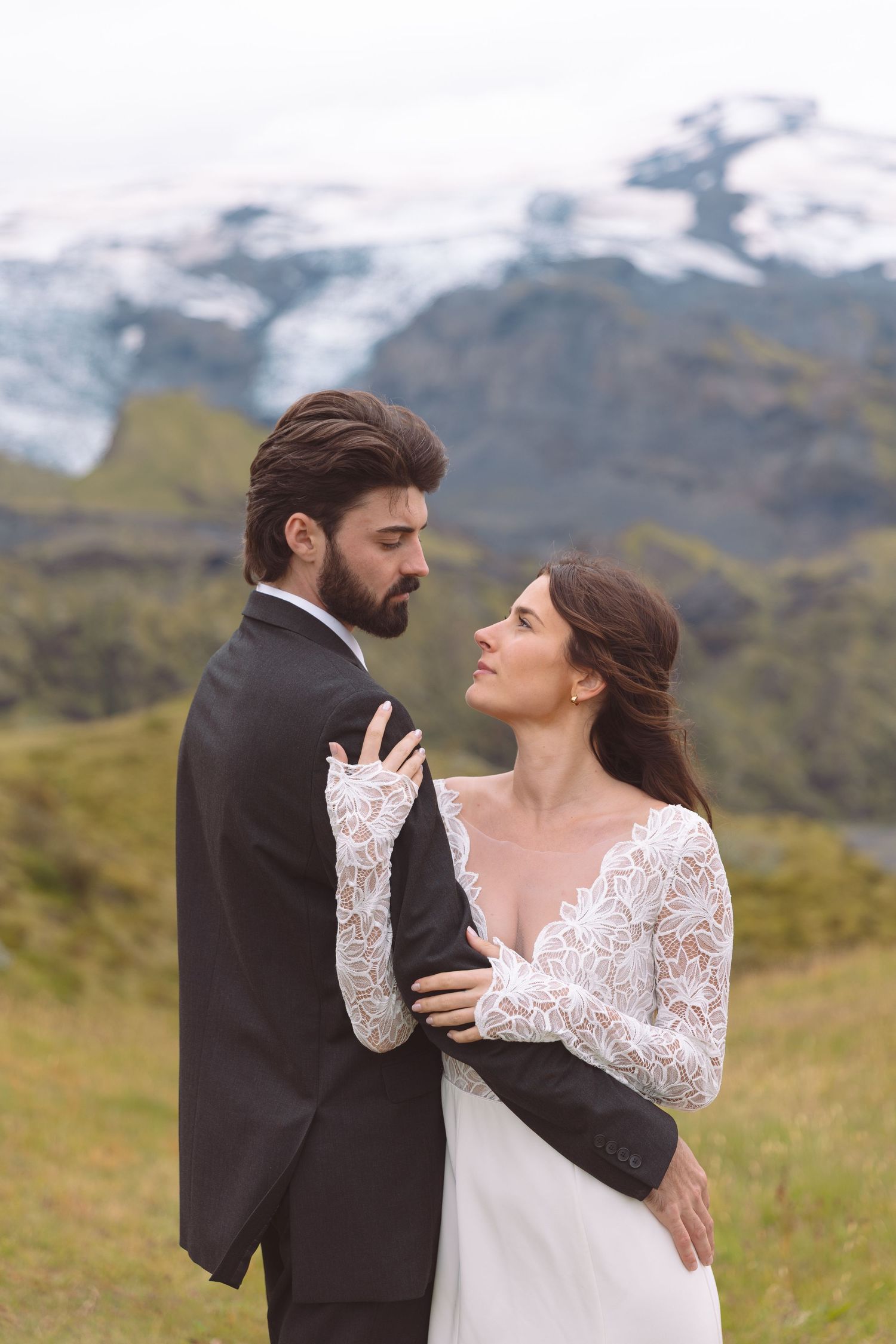 Romantic bride and groom sharing a tender gaze while embracing in front of snowy mountains.