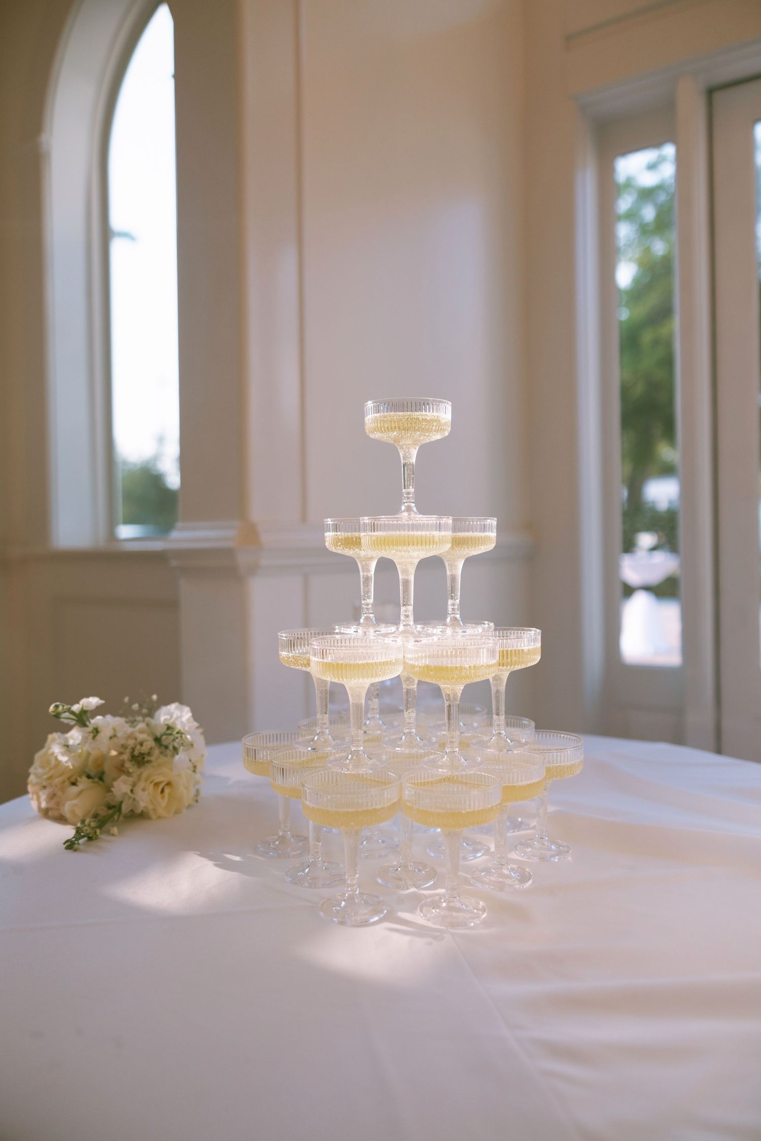 Elegant champagne tower with coupe glasses on a white tablecloth at a wedding.