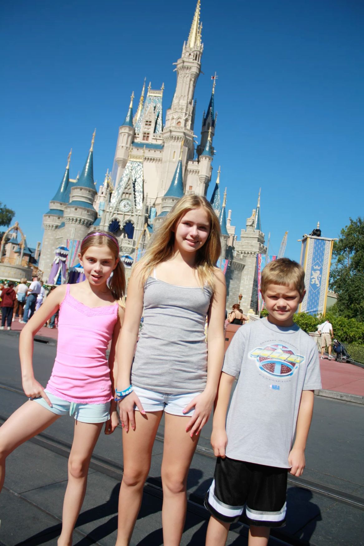 Three children smiling in front of Cinderella Castle at Walt Disney World Magic Kingdom on a sunny day.