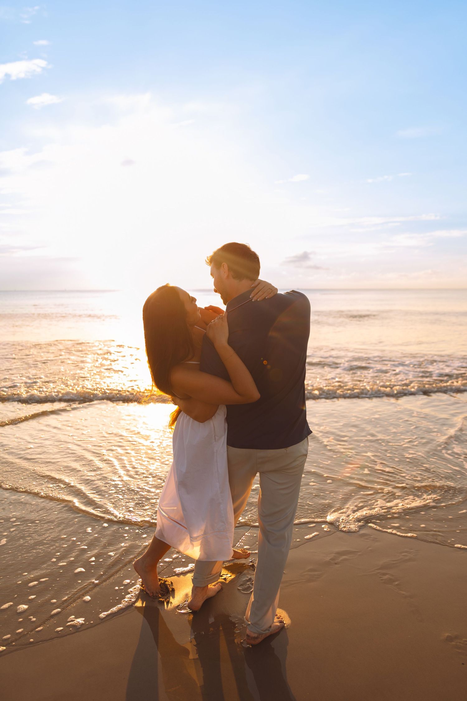 Romantic couple embracing on a sandy beach at golden sunset with ocean waves behind them.