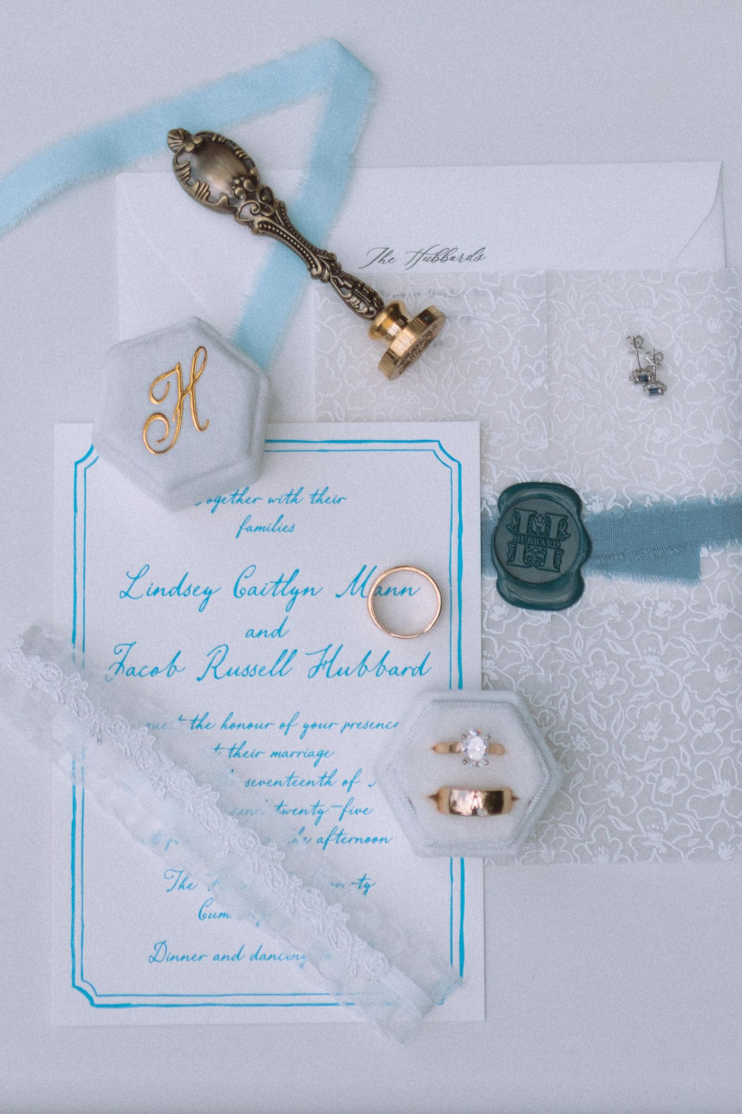 Elegant blue and white wedding invitation suite with rings, wax seal, and bridal accessories.