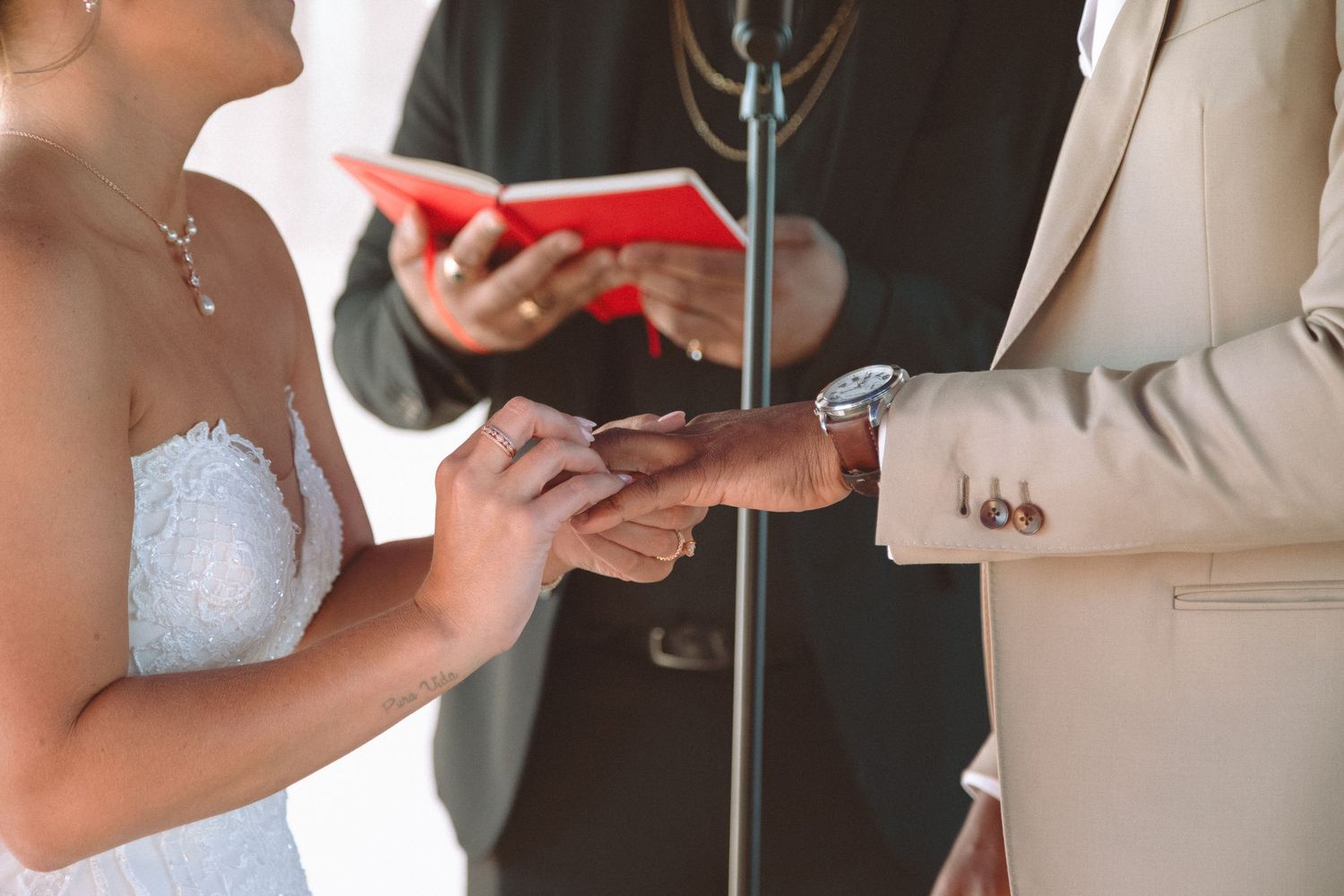 Close-up of bride placing wedding ring on grooms hand during ceremony officiated by minister.