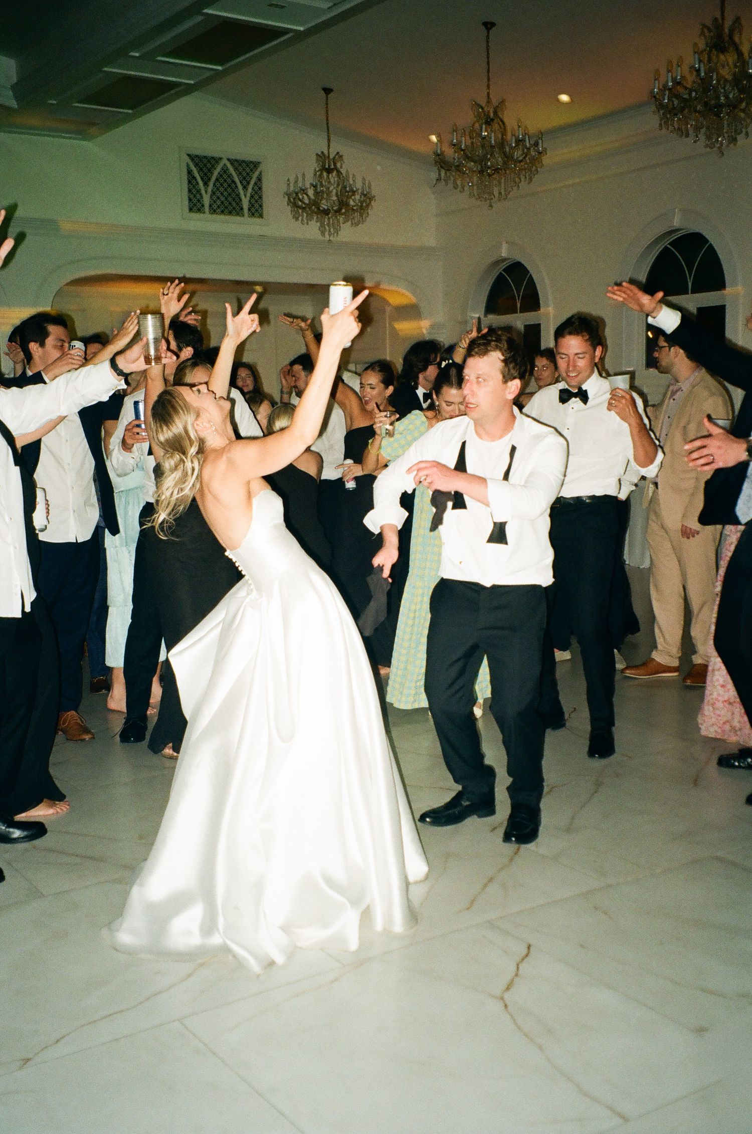 Bride in white satin gown dancing energetically with groom at elegant wedding reception.