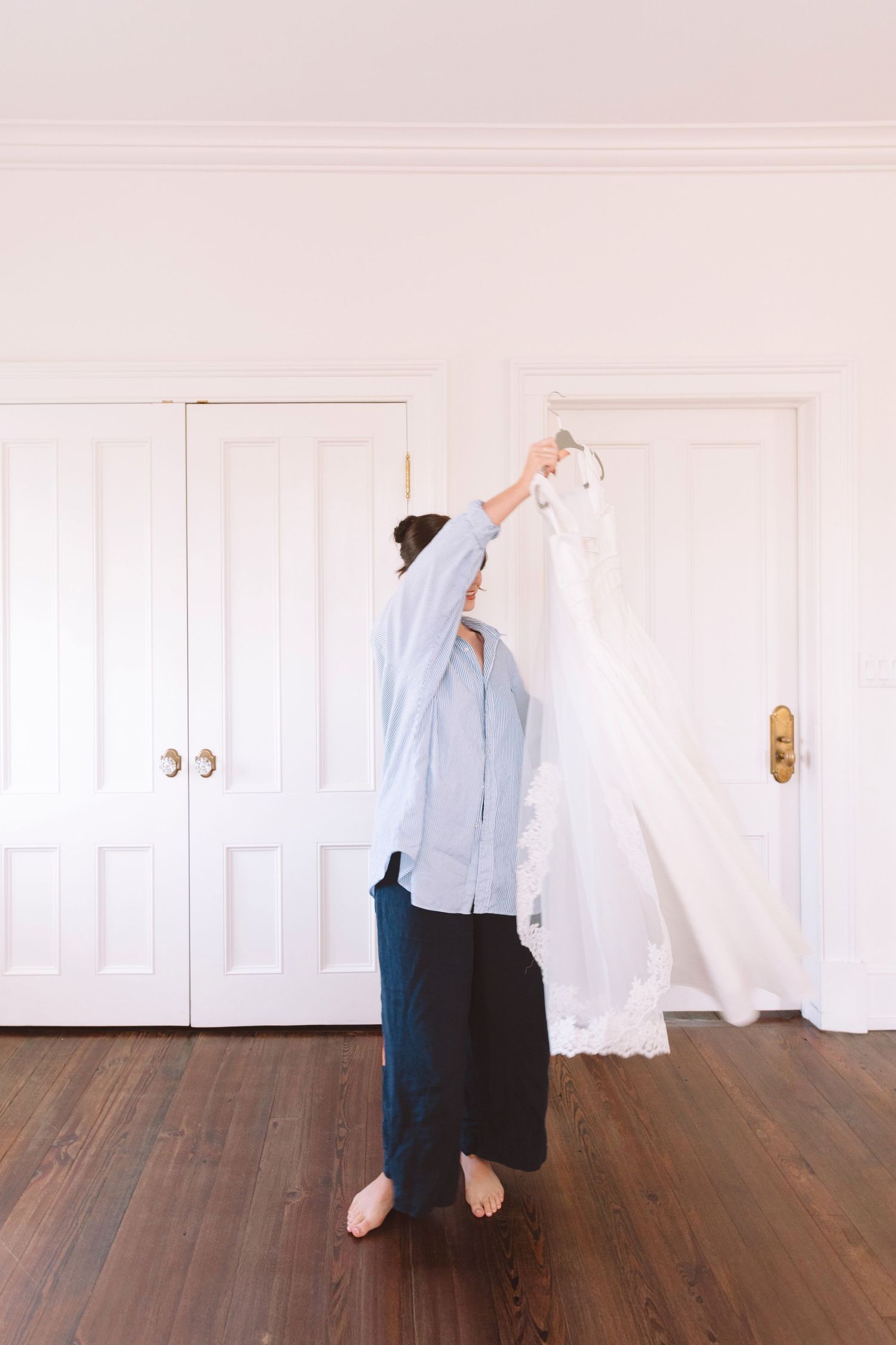 Person holding up a white wedding dress against closet doors in a bright white room.