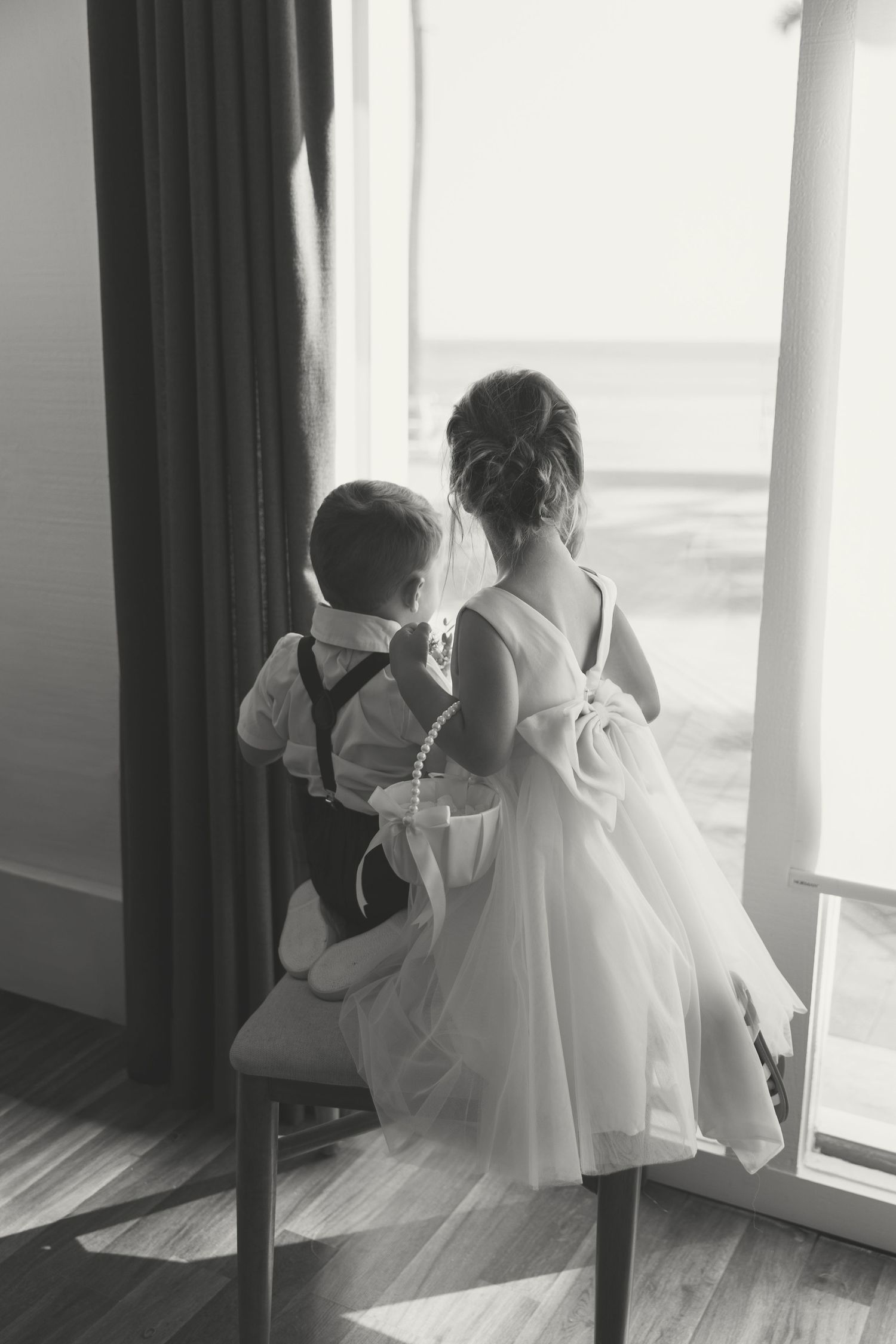 Black and white photo of flower girl and ring bearer looking out window at beach.