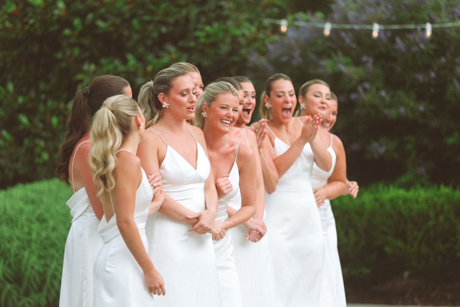 Bridesmaids in white dresses laughing together outdoors at a wedding celebration.