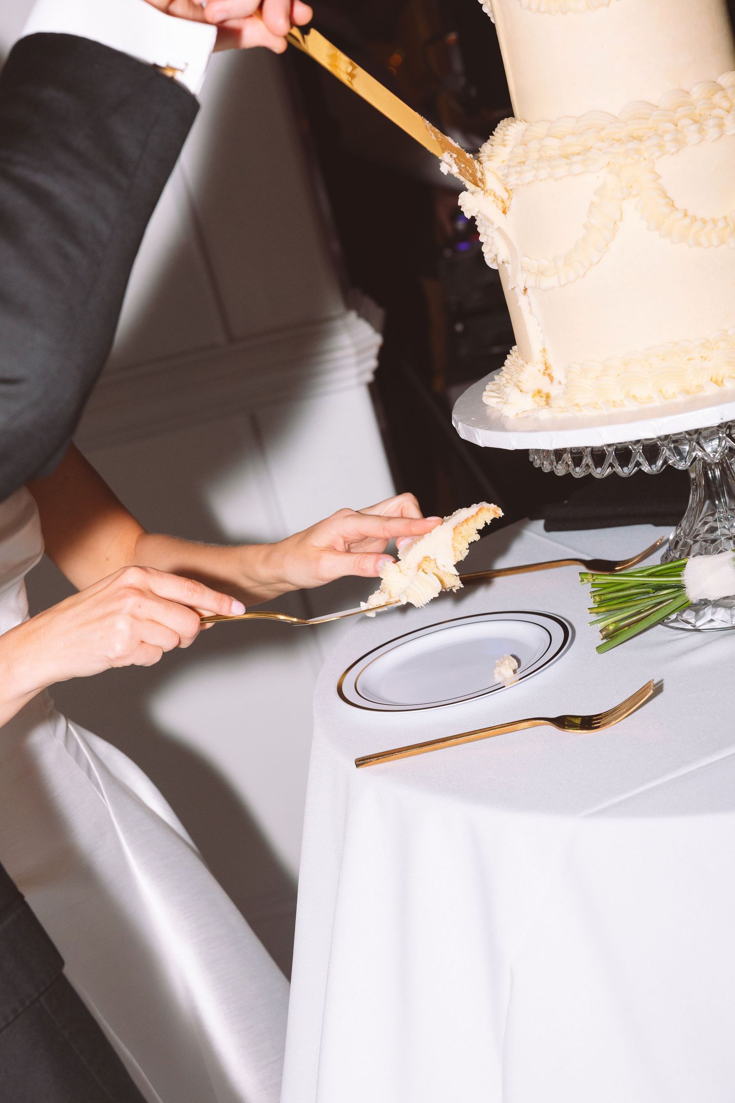 Bride and groom cutting a white three-tier wedding cake with gold utensils at their reception.