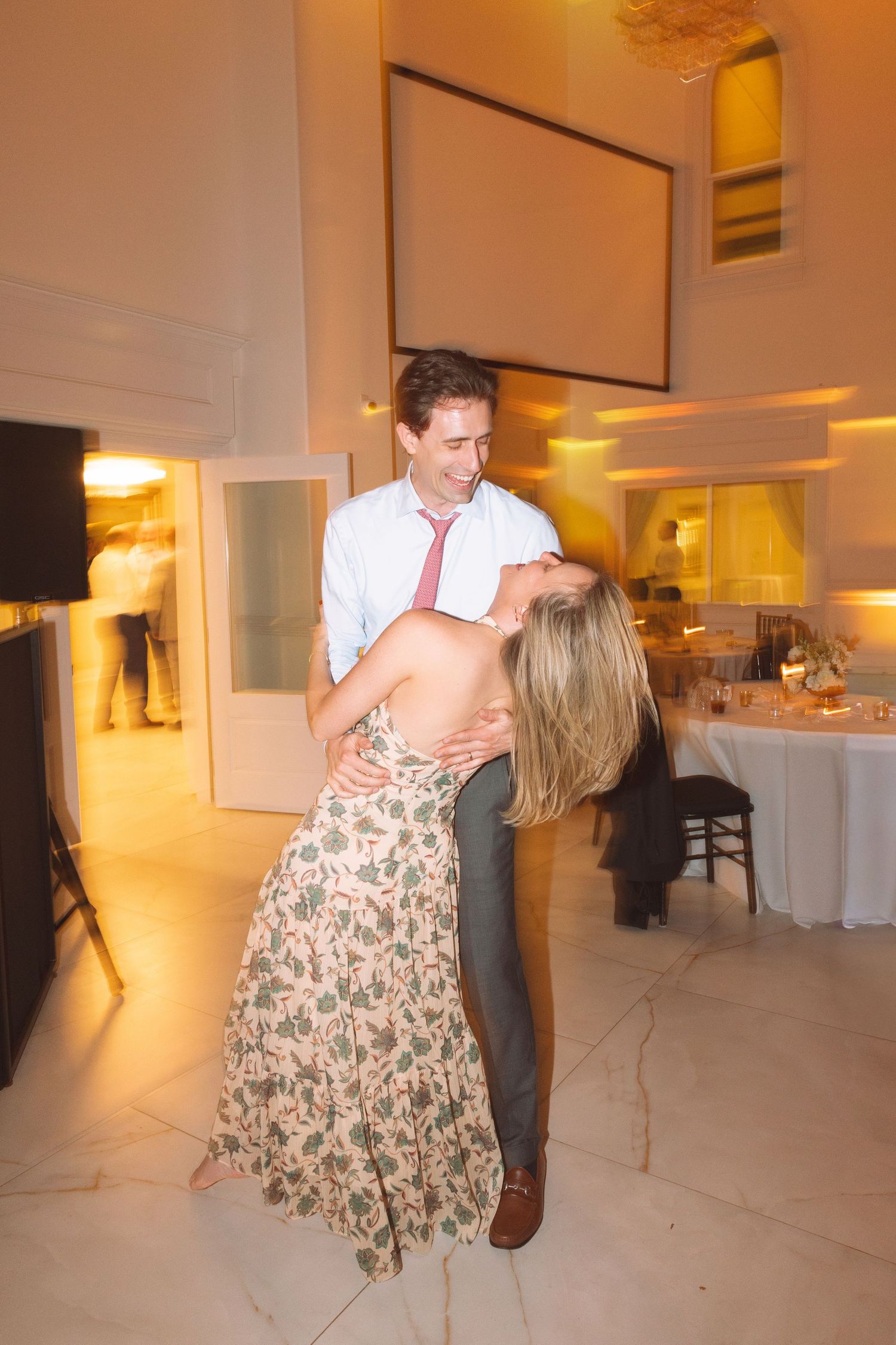 Couple dancing and dipping at a wedding reception in an elegant white venue with warm lighting.