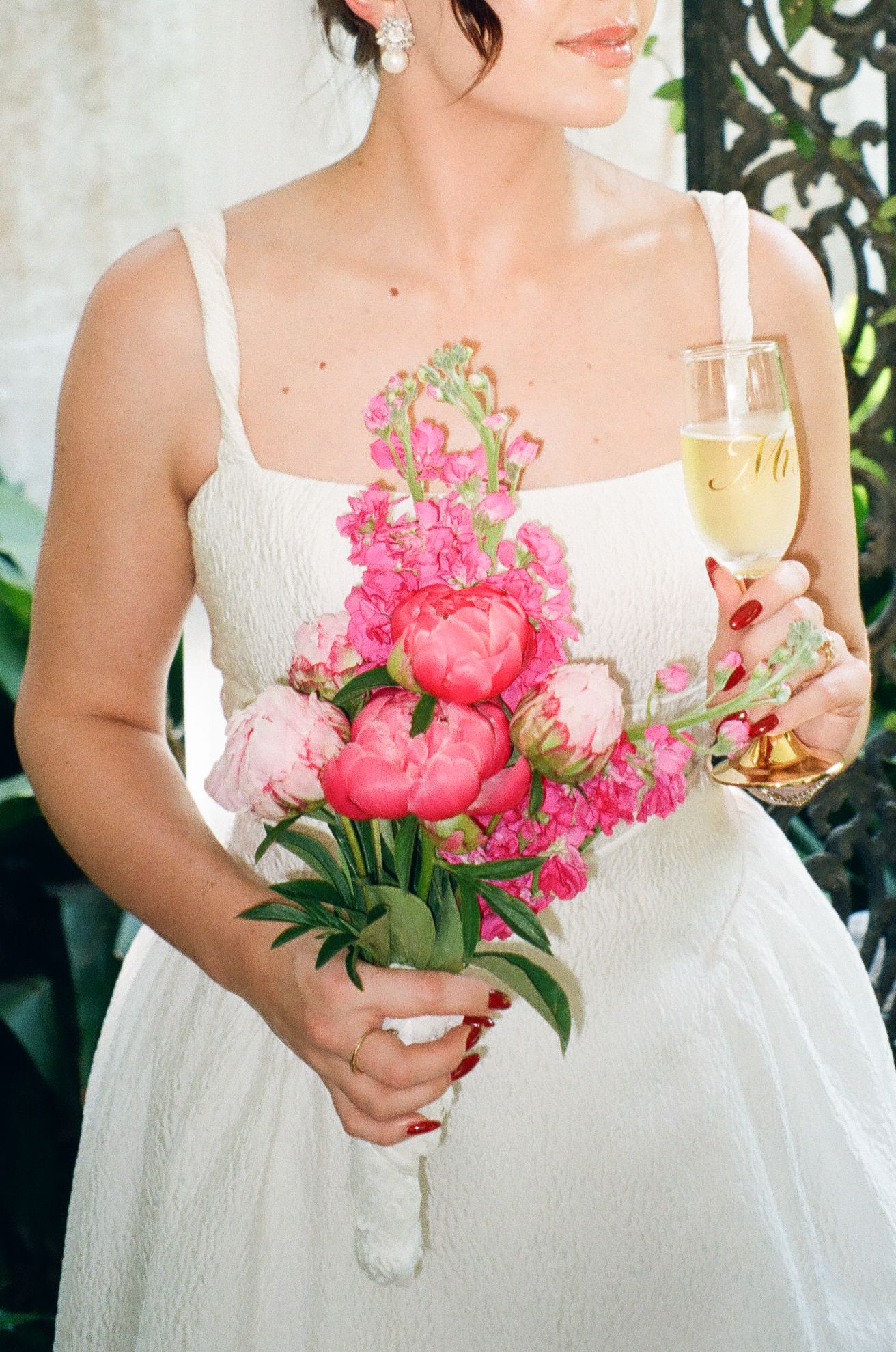 Bride in white dress holding pink peony bouquet and champagne glass at wedding celebration.