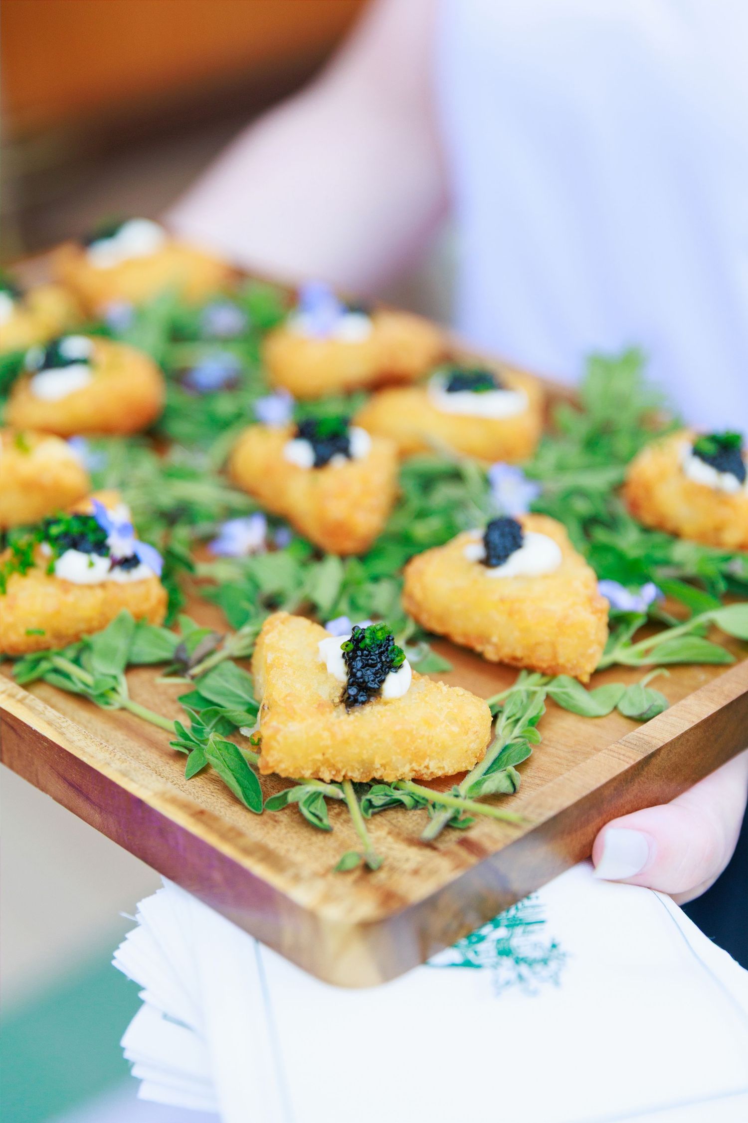 Golden fried appetizers topped with cream cheese and black caviar on fresh greens served on a wooden board.