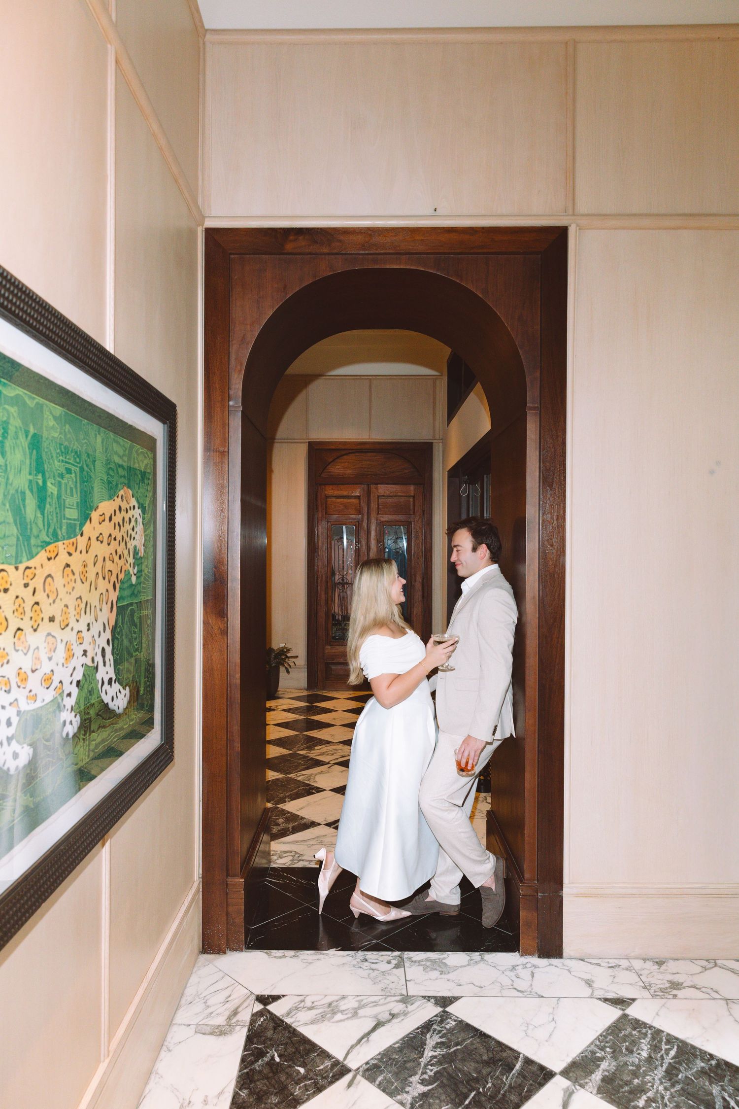 Elegant couple embracing in a luxurious hotel hallway with arched doorway and marble floors.