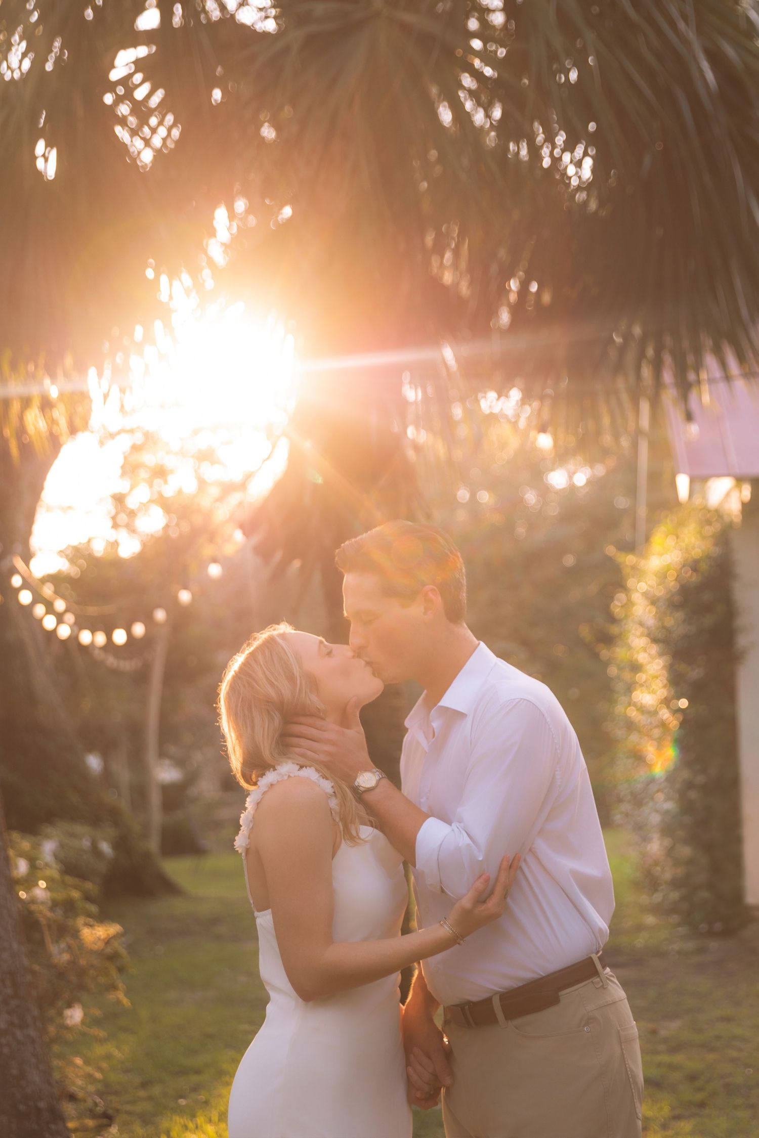 Couple sharing a romantic kiss at golden sunset under palm trees.